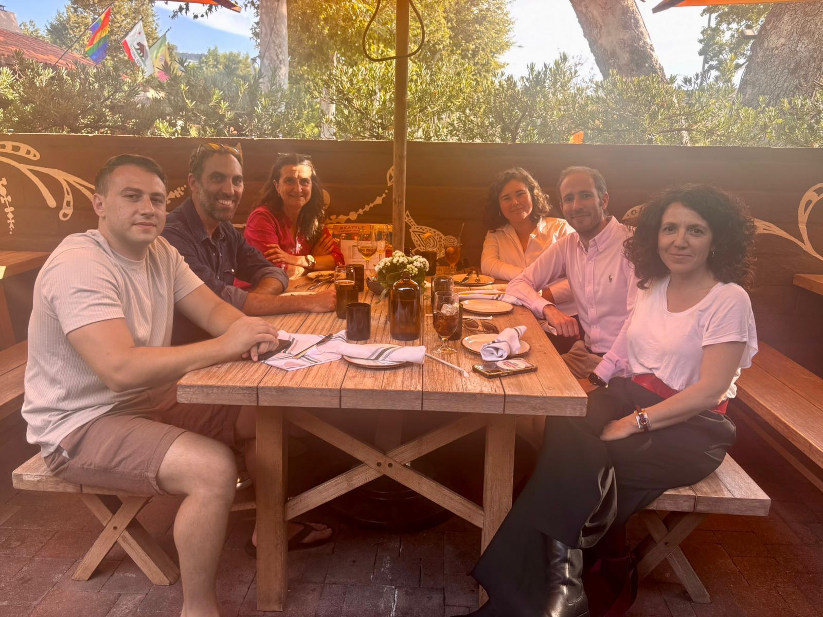Un grupo de seis personas disfruta de una comida al aire libre en una mesa acogedora.
