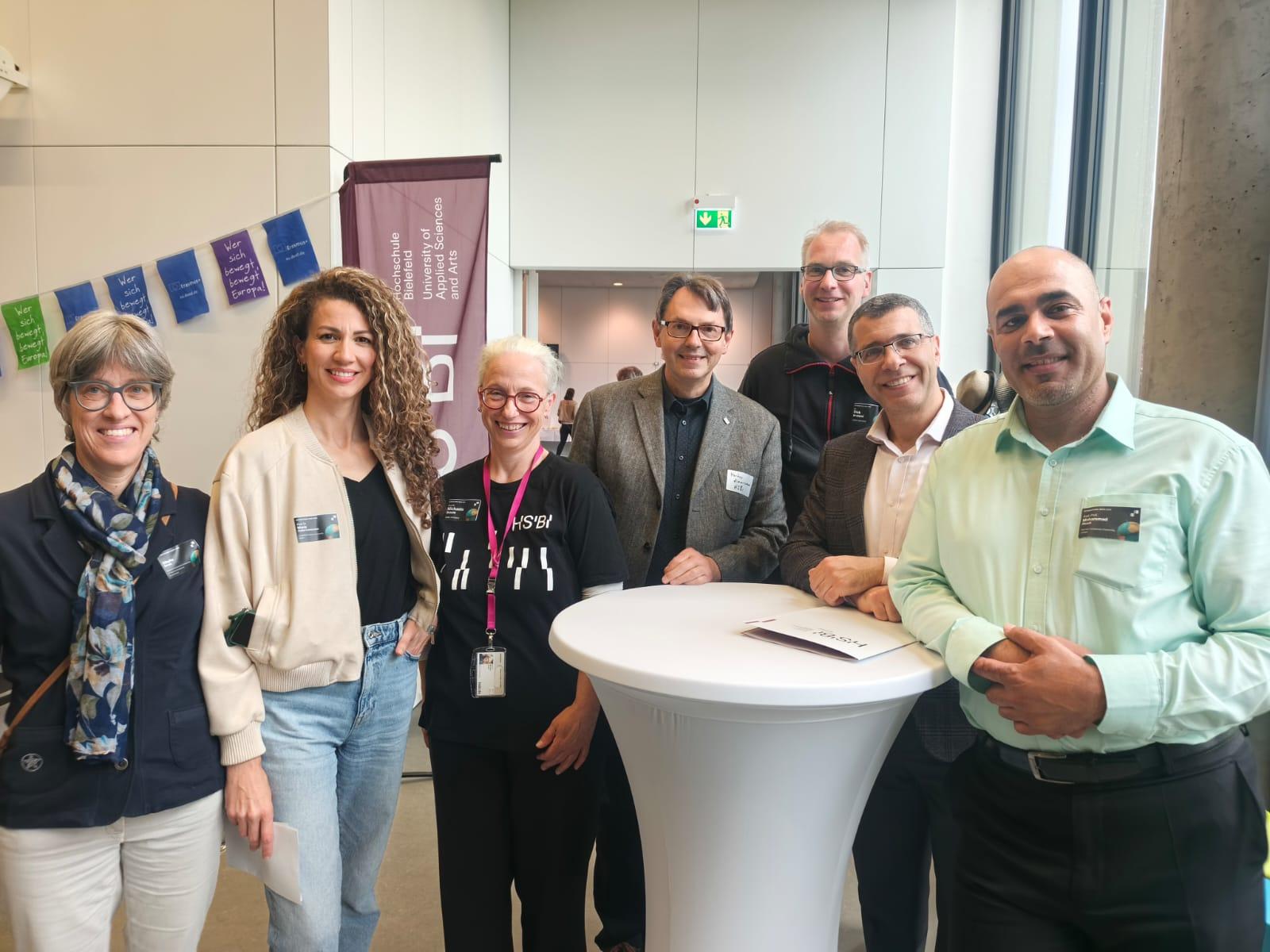 Un grupo de siete personas posando juntas en un evento con mesas y decoración de fondo.