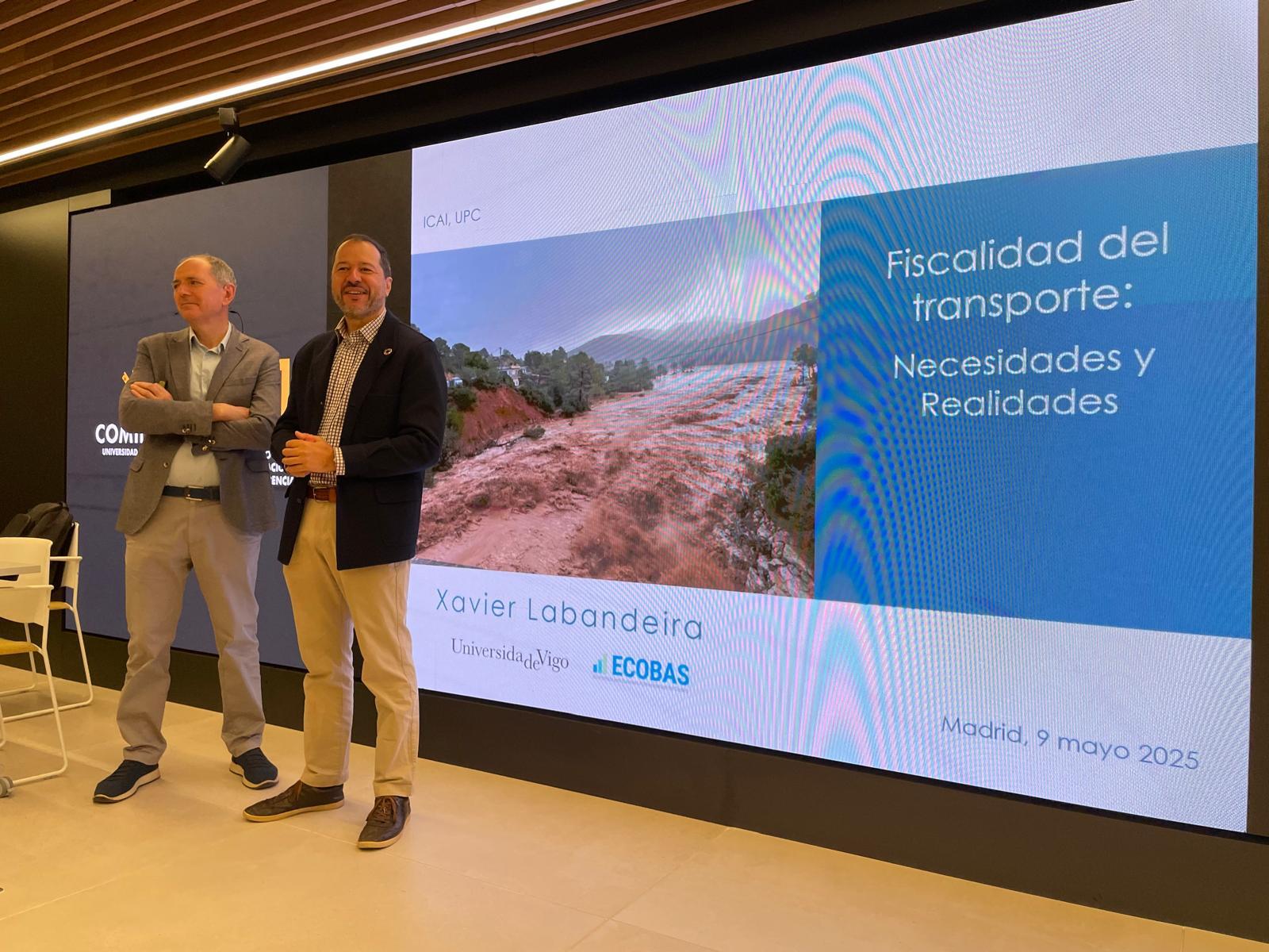 Dos hombres de pie frente a una pantalla que muestra una presentación sobre la fiscalidad del transporte.