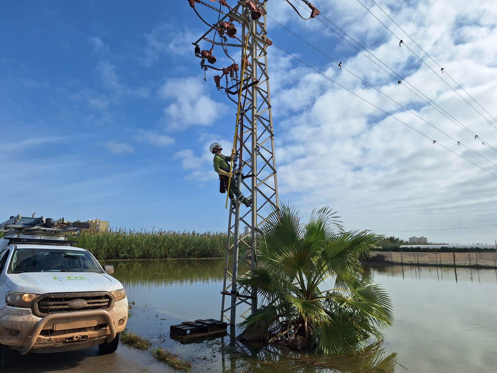 Un trabajador está subiendo por un poste eléctrico cerca de un área inundada.