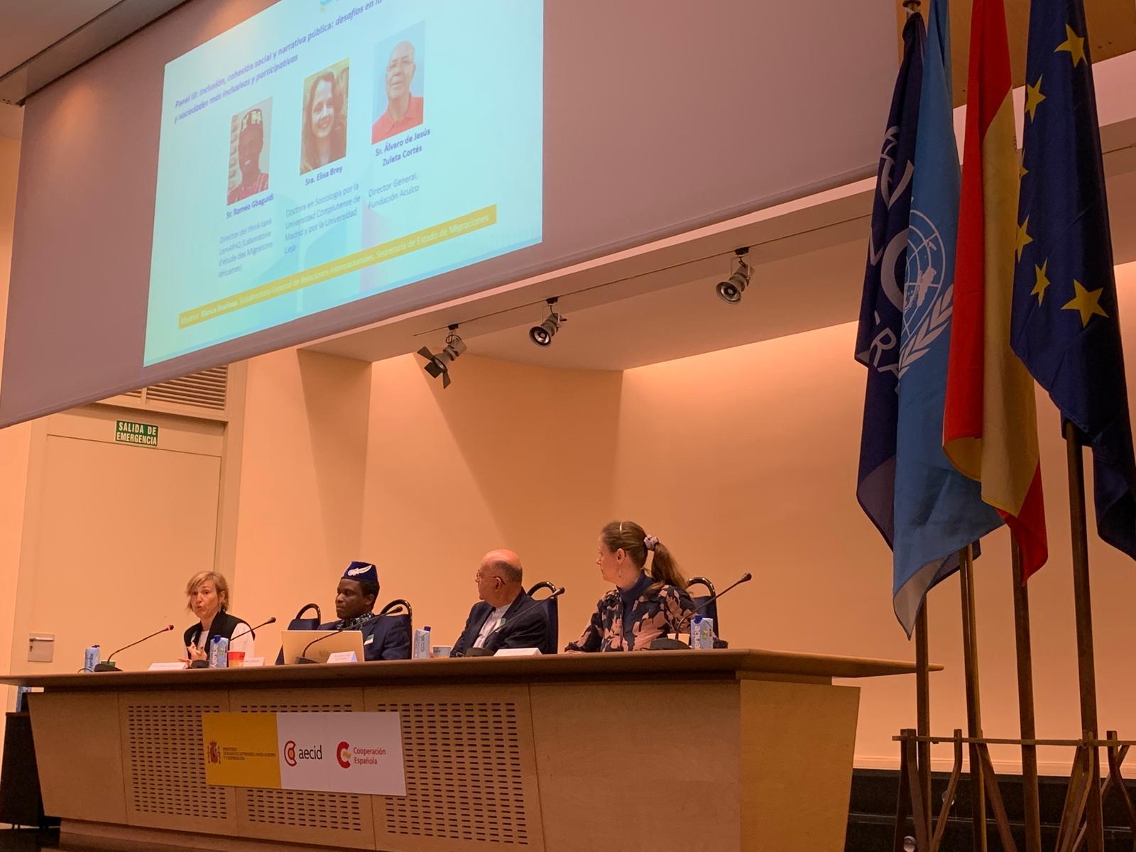 Una mesa redonda con cuatro ponentes en un escenario, rodeados de banderas.