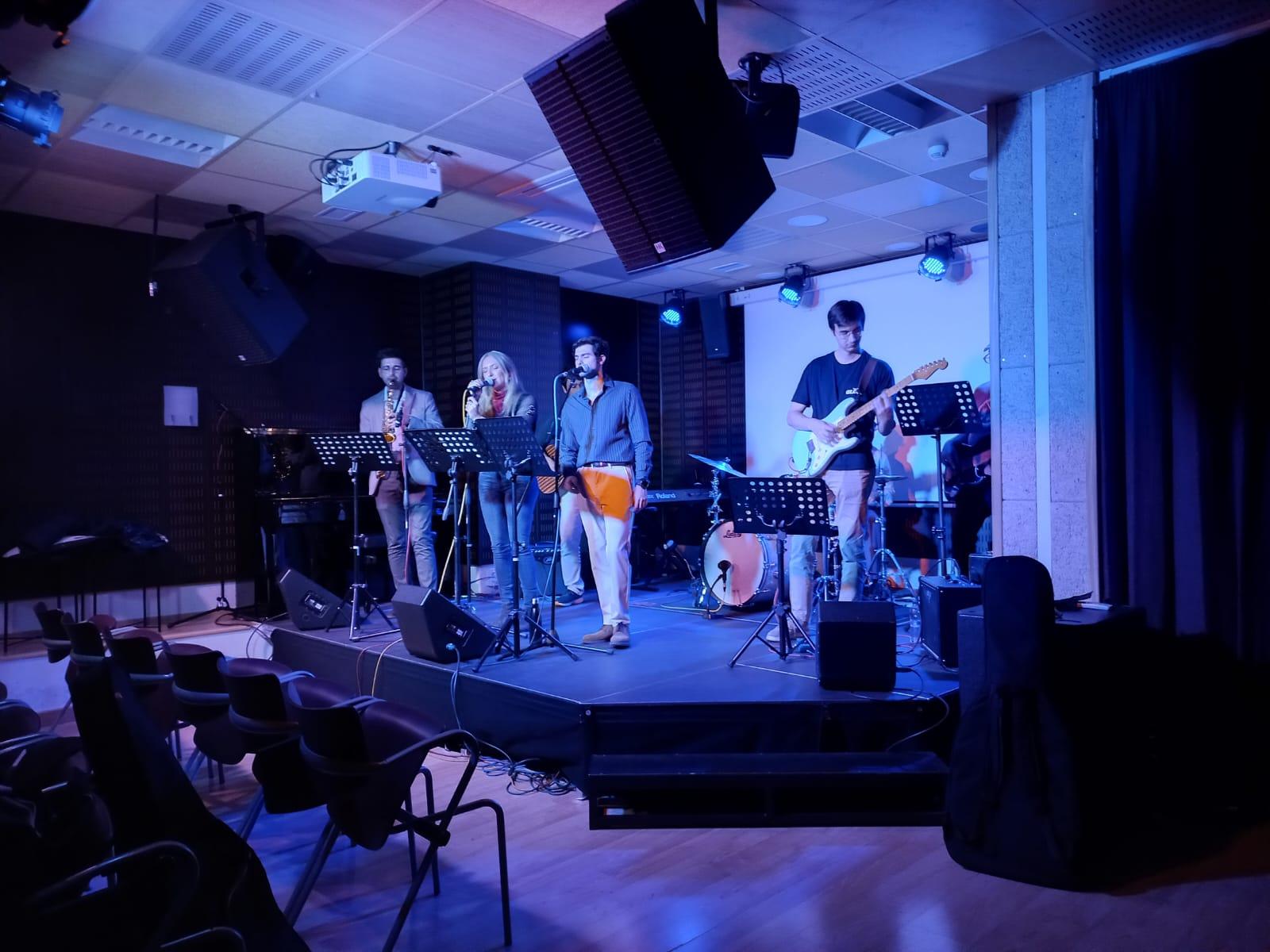 Una banda de música se presenta en un escenario iluminado con luces azules y violetas.