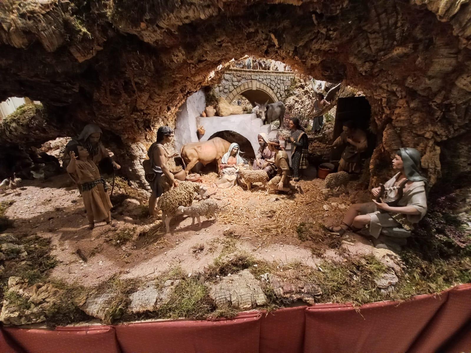 La imagen muestra un belén con figuras que representan el nacimiento de Jesús en un entorno natural.