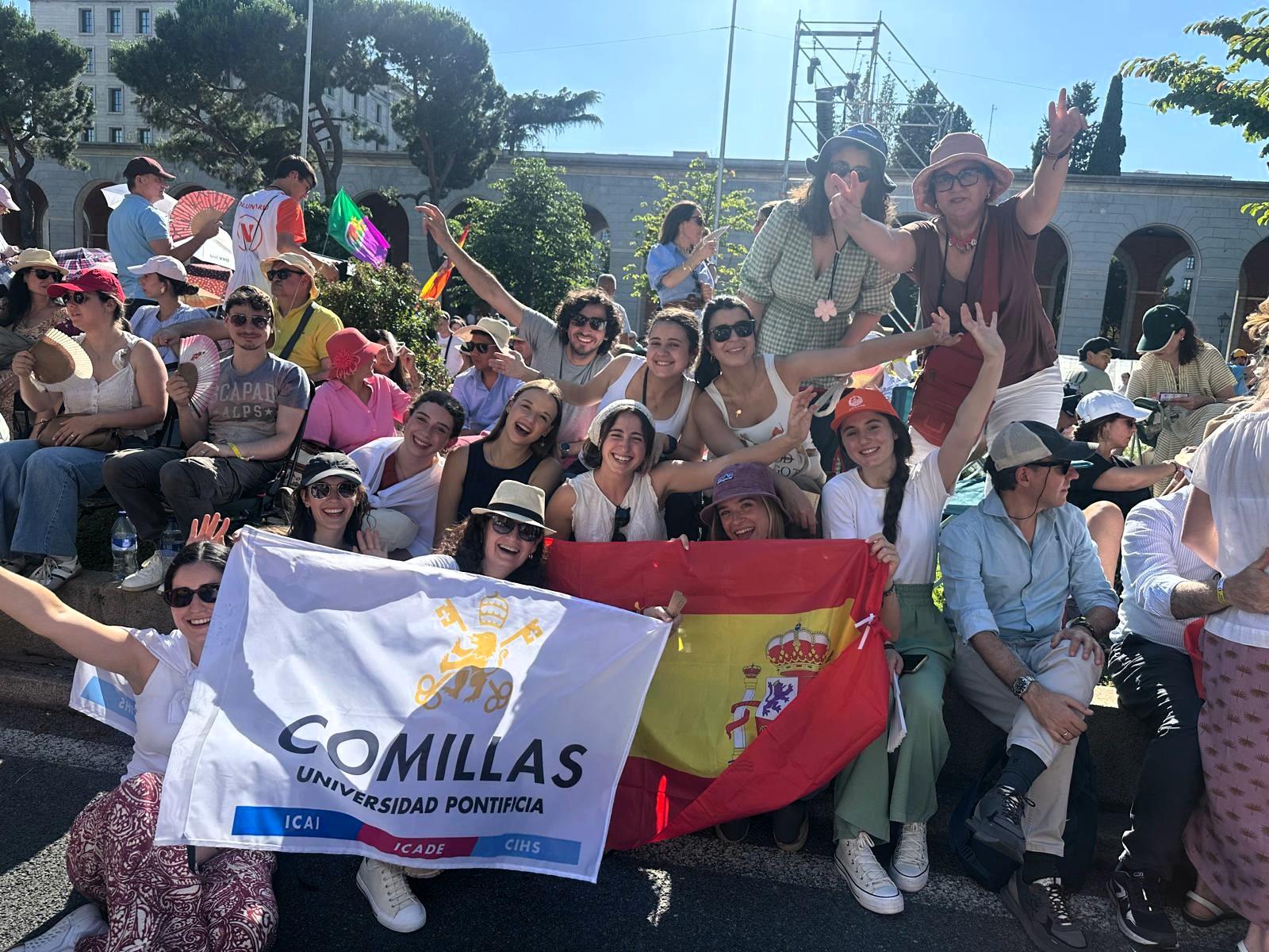 Grupo de estudiantes de la Universidad Pontificia Comillas posando con banderas y sonriendo en un evento al aire libre.