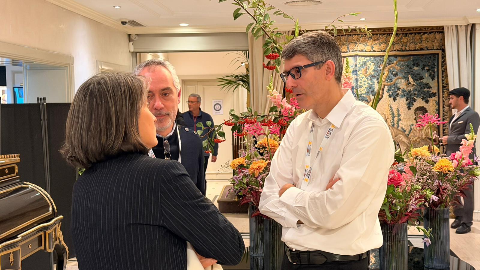 Tres personas conversan en un ambiente decorado con flores.