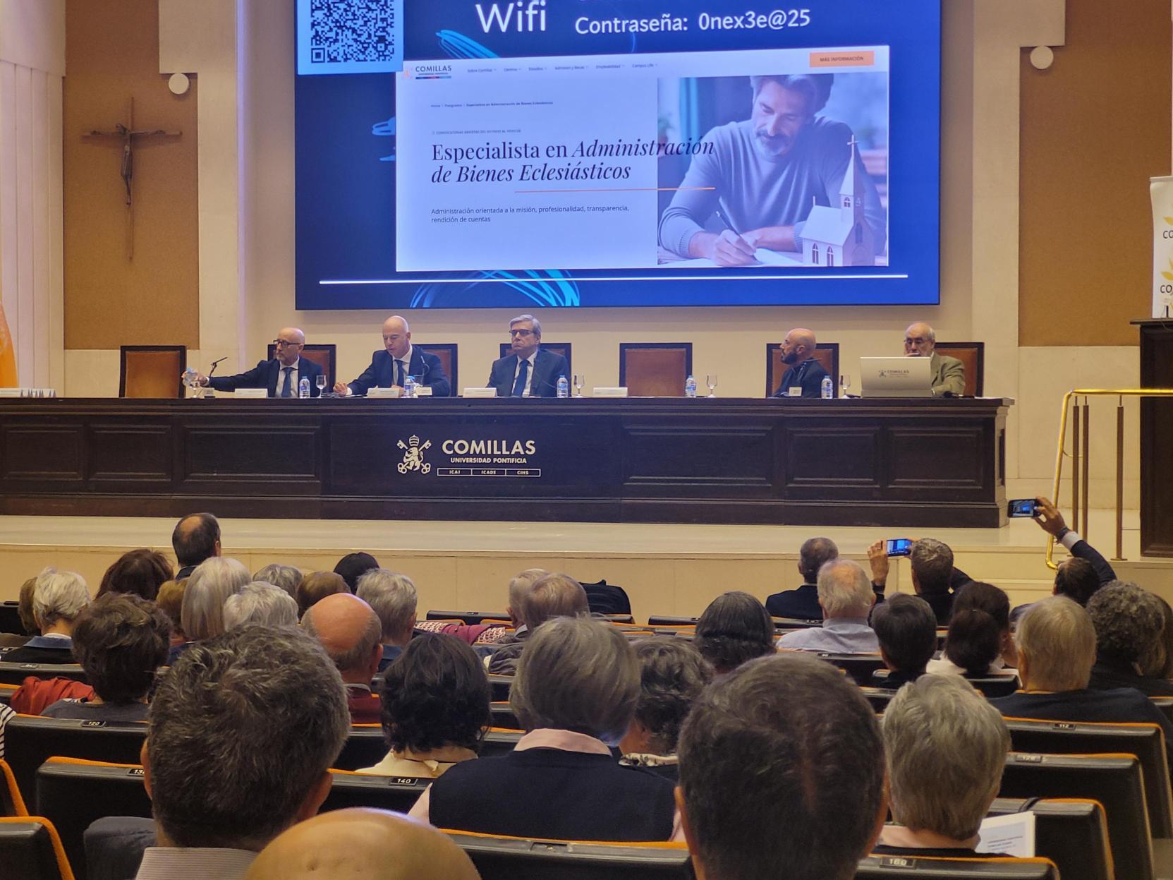 Un evento académico con un panel de expertos discutiendo sobre administración de bienes eclesiásticos frente a un gran público.