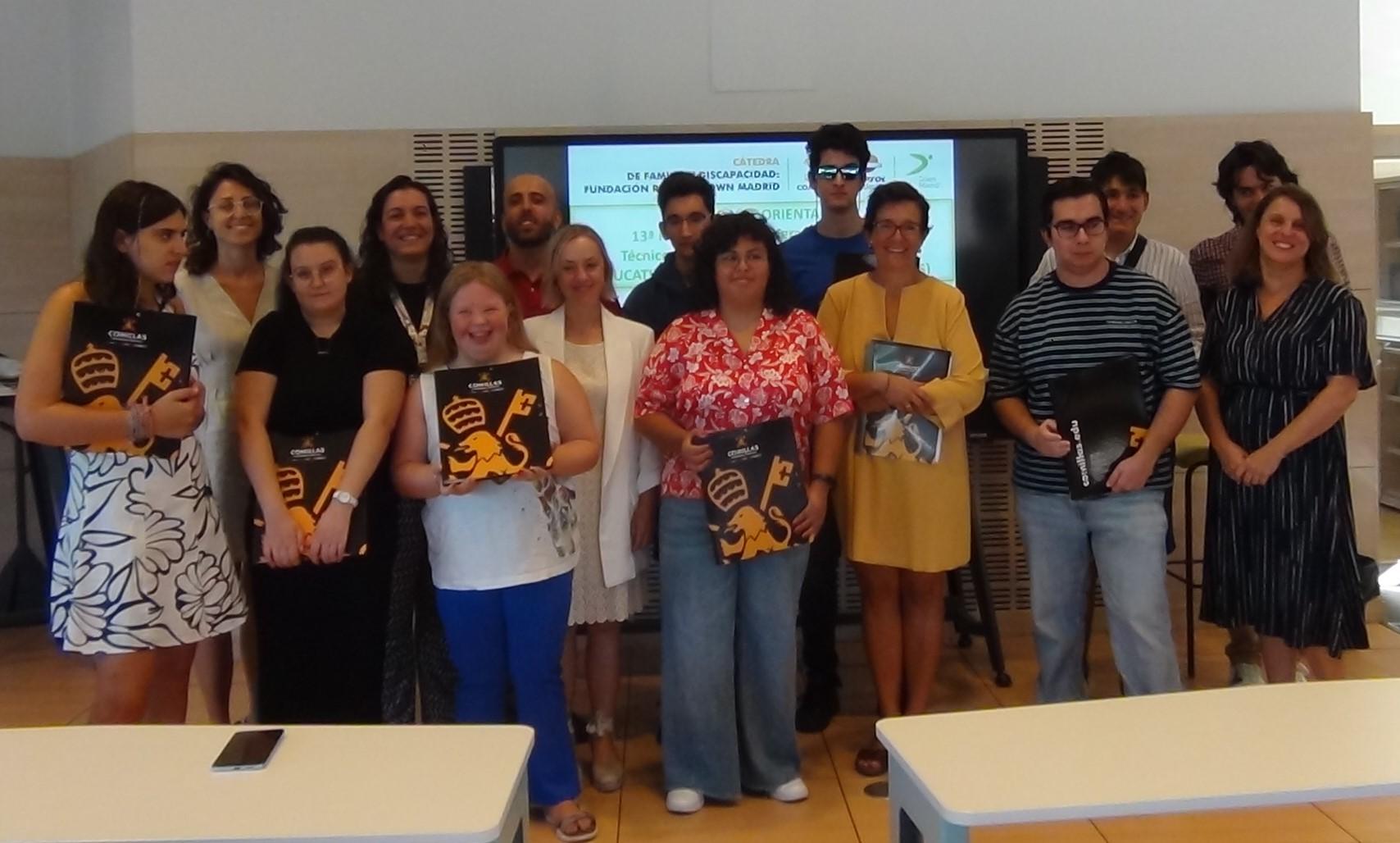 A group of people standing in a room with a presentation screen in the background, some holding books and promotional materials.