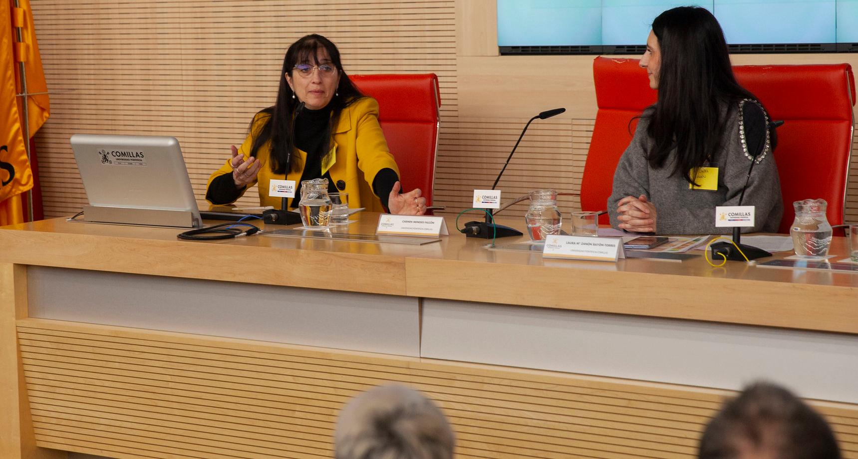 Dos mujeres están sentadas en una mesa de conferencia dando una presentación.