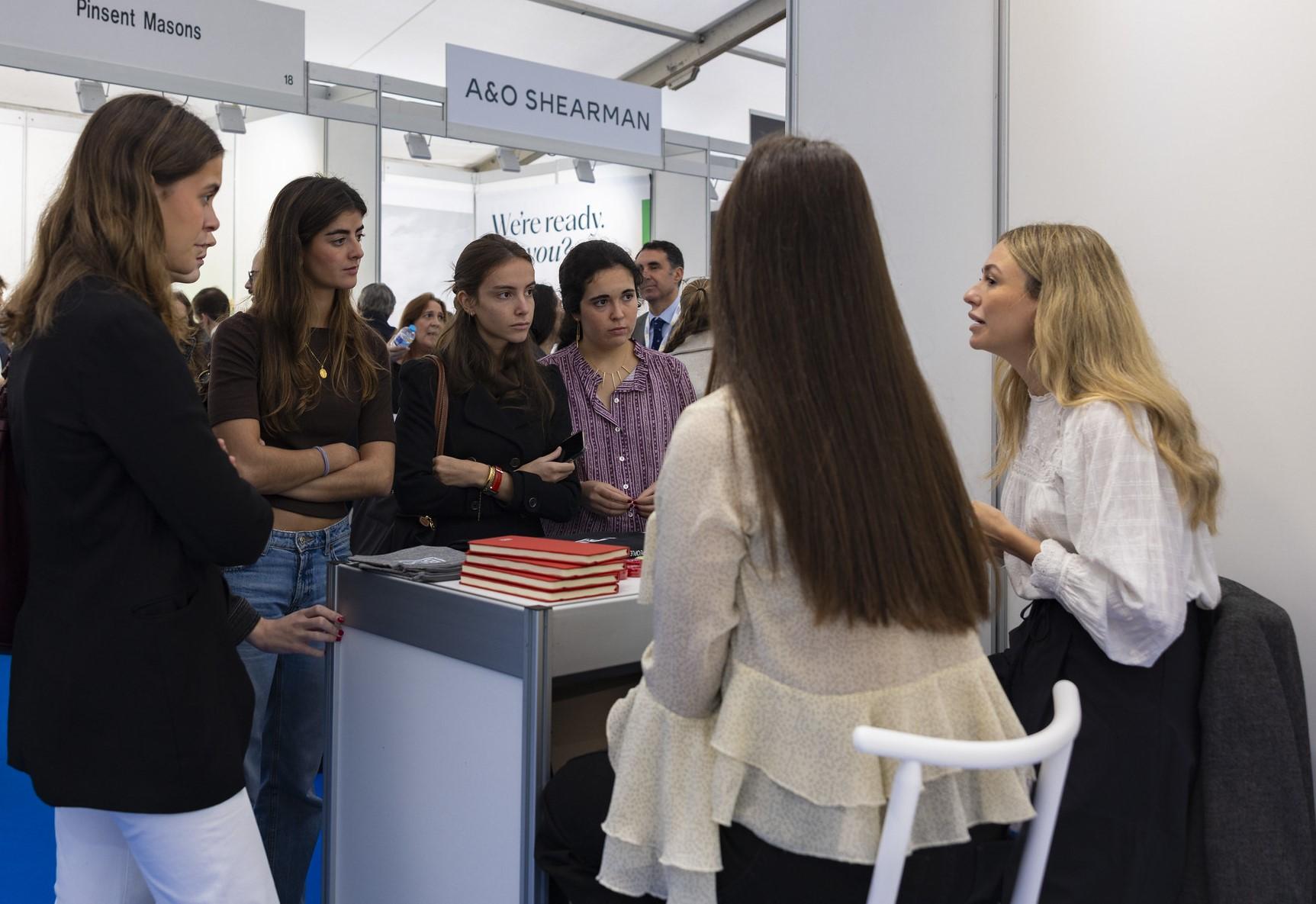 Un grupo de mujeres jóvenes está conversando en un evento, con atención hacia una mujer que les habla.