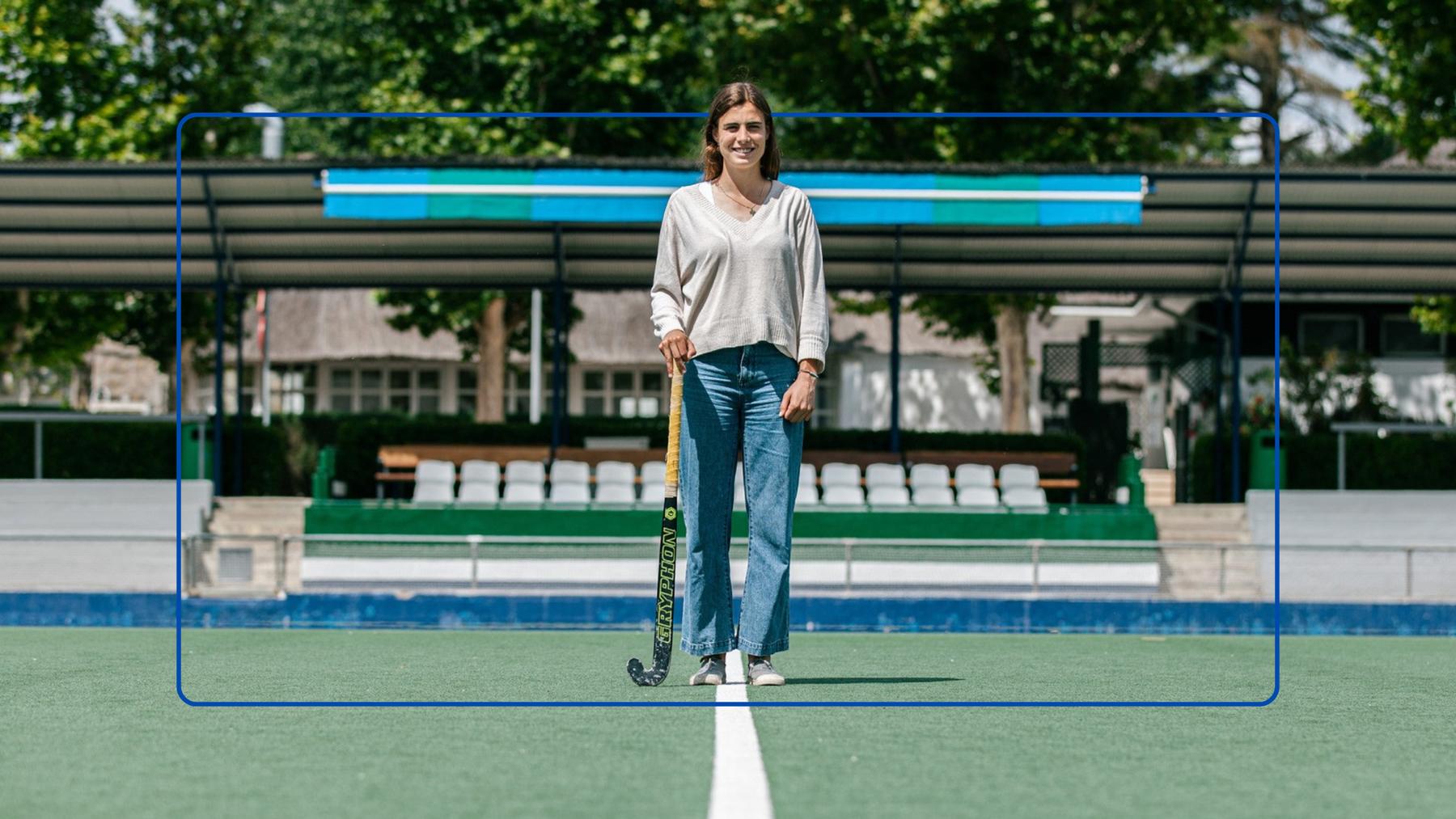 Una mujer sonriente de pie en una cancha de hockey sosteniendo un stick.