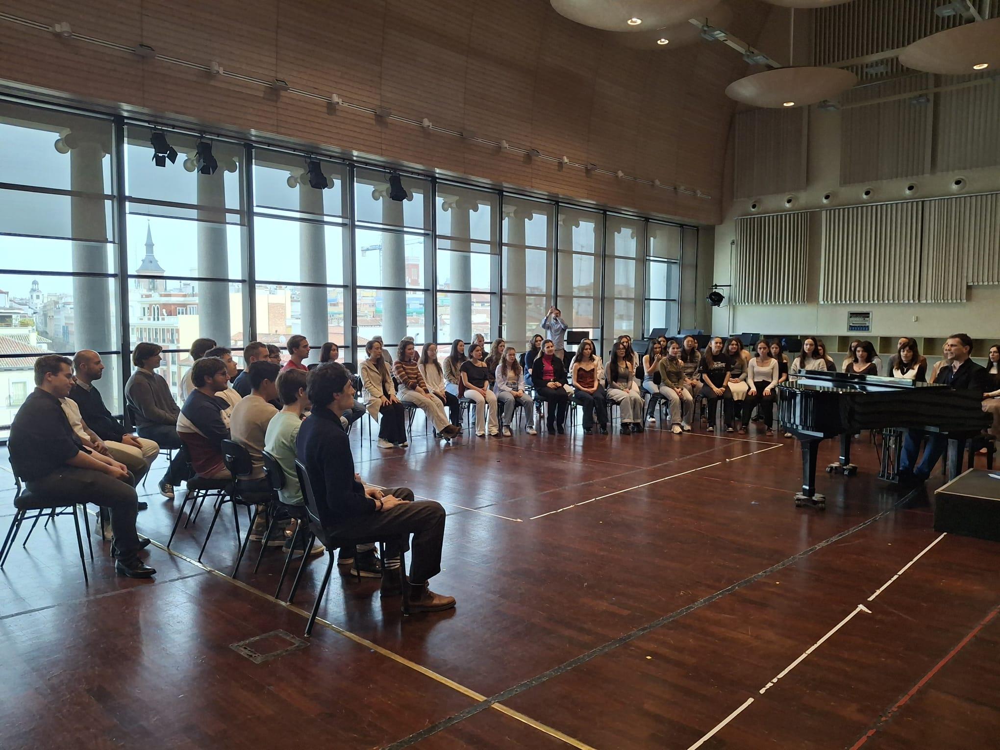 Un grupo numeroso de personas se sienta en un salón mirando hacia un pianista que toca.