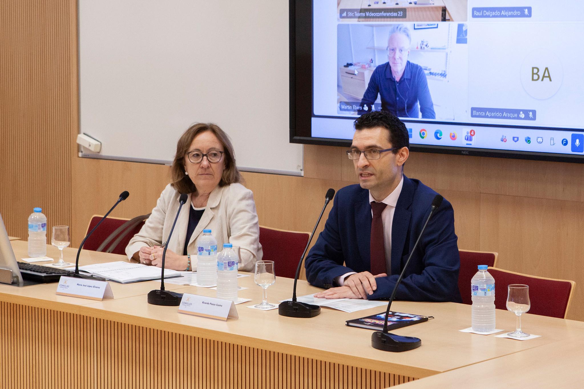 Una presentación formal con dos oradores frente a una audiencia virtual en una sala de conferencias.