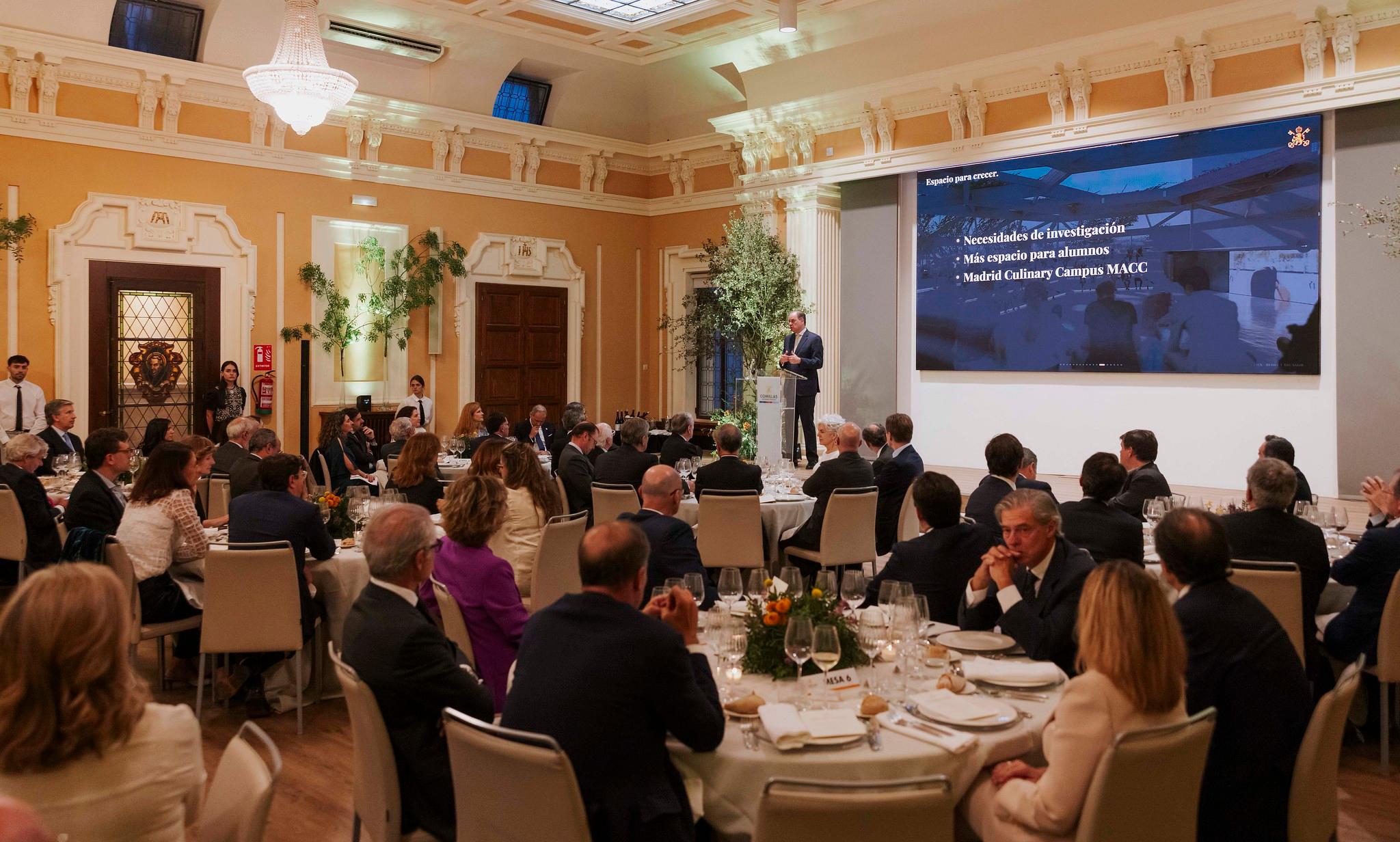 Una cena elegante con un orador en un escenario frente a un público atento.