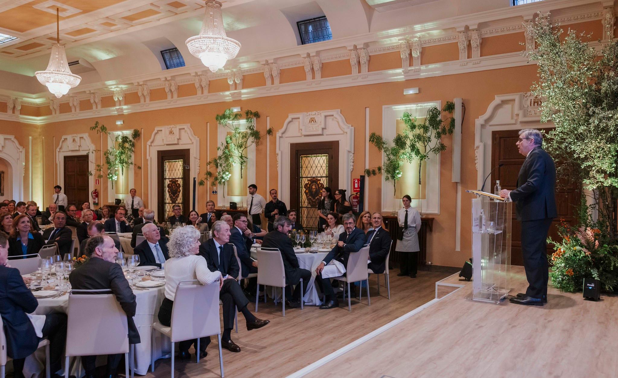 Un hombre habla frente a un grupo de personas en un evento social elegante.