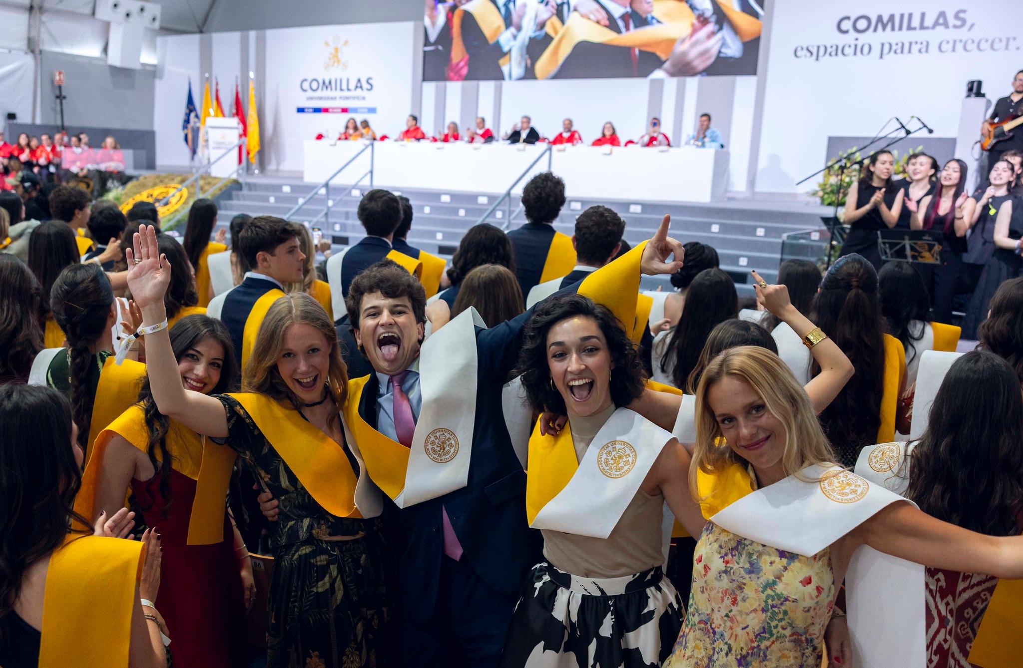 Un grupo de graduados celebra con alegría en una ceremonia académica, luciendo togas y birretes en un ambiente festivo.