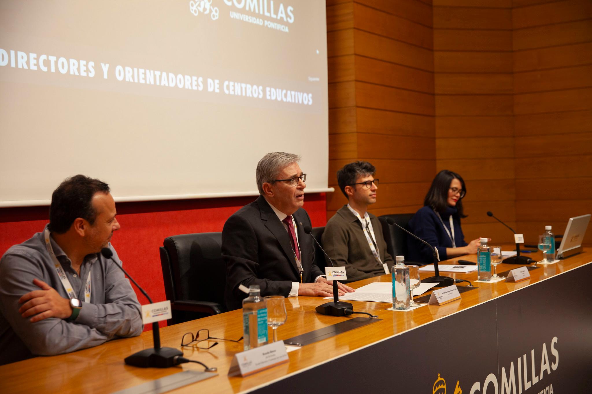 Cuatro personas sentadas en un panel en una conferencia, con carteles con nombres y logos en la mesa frente a ellos.