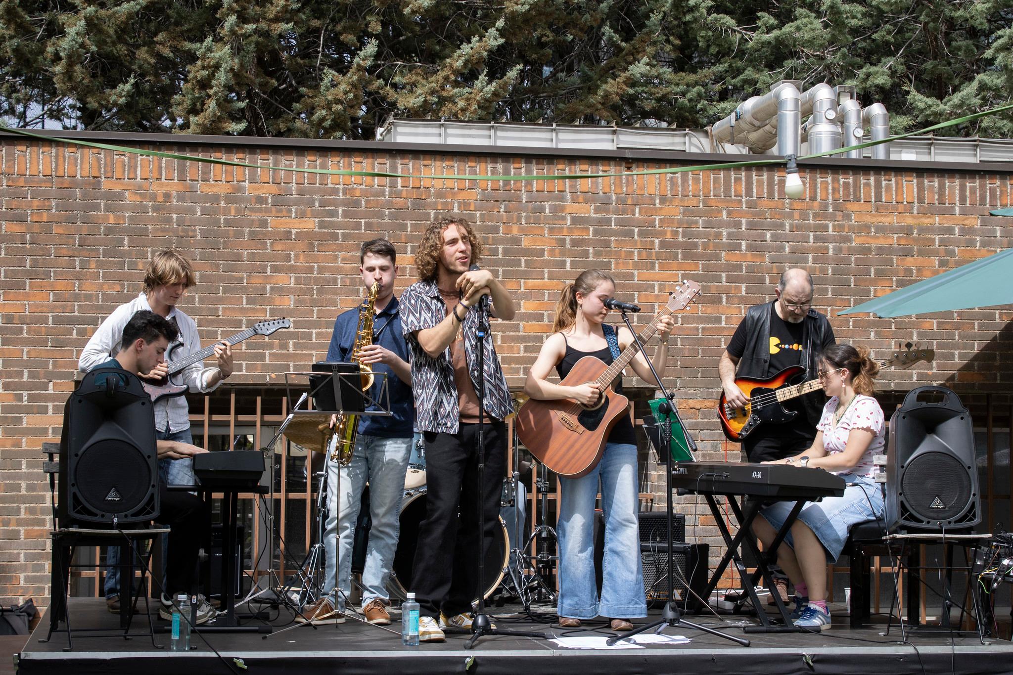 Un grupo de músicos se presenta en un escenario al aire libre, tocando diferentes instrumentos.