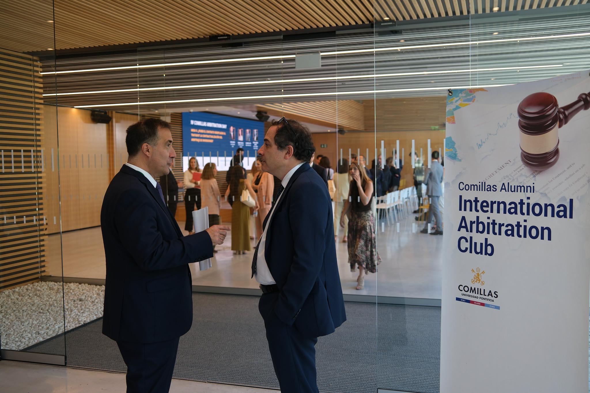 Dos hombres conversan en un evento relacionado con el Club de Arbitraje Internacional de Alumni de Comillas.