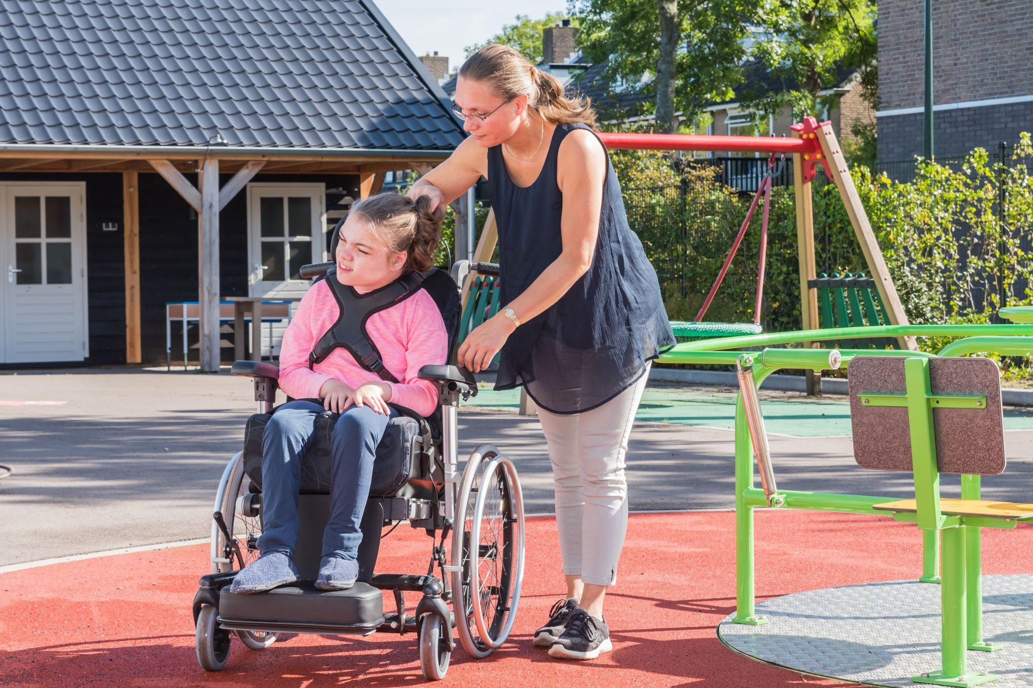 Una mujer está empujando una silla de ruedas con una niña en un parque infantil.