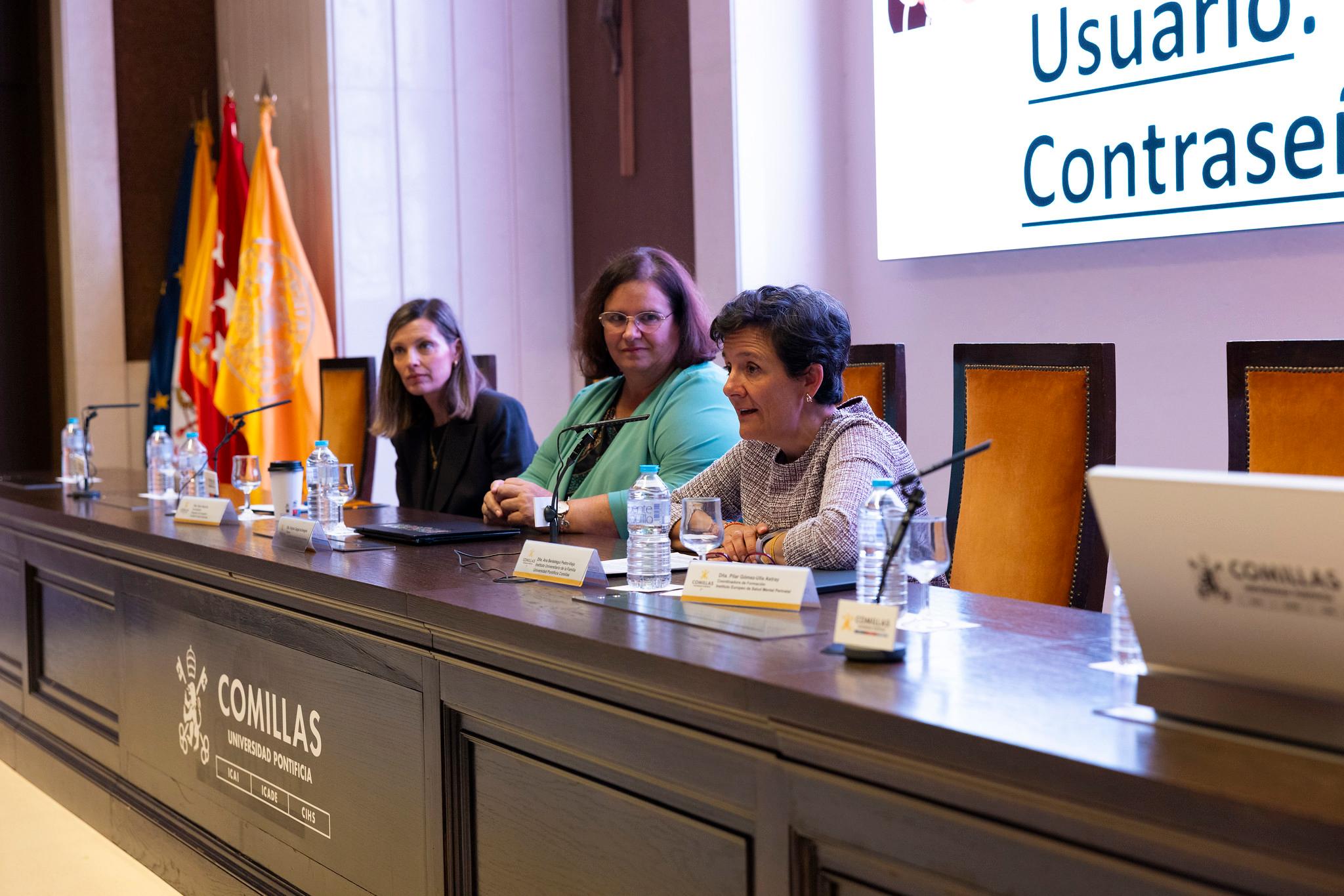 Tres mujeres participan en un evento en una mesa de conferencias en un auditorio.