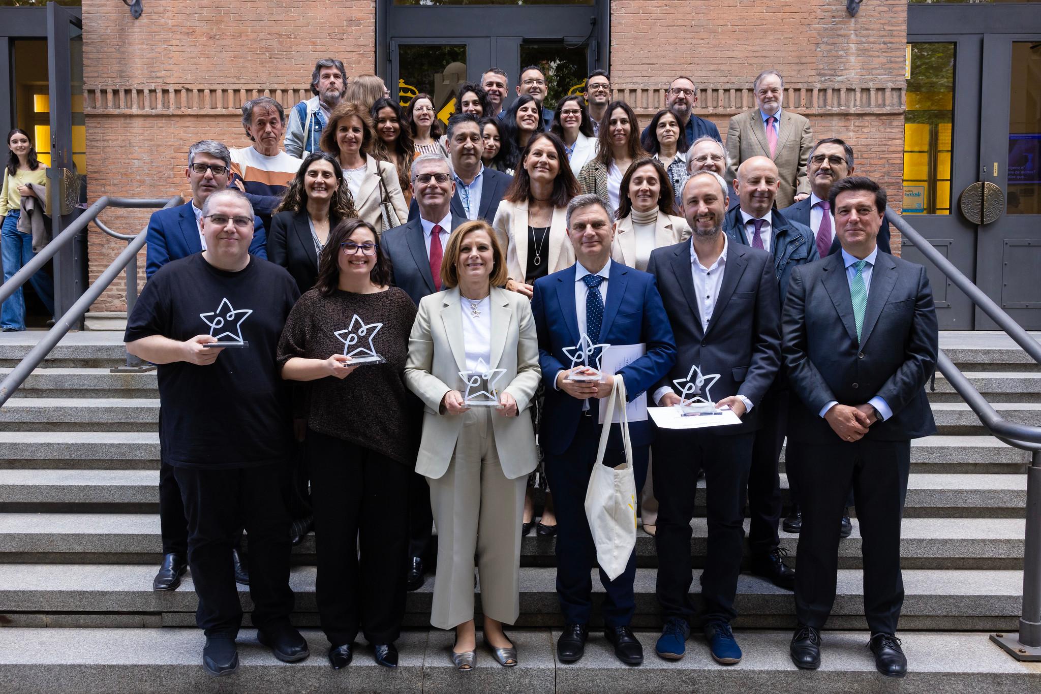 Un grupo de personas posando en un evento, sosteniendo trofeos en una escalera.
