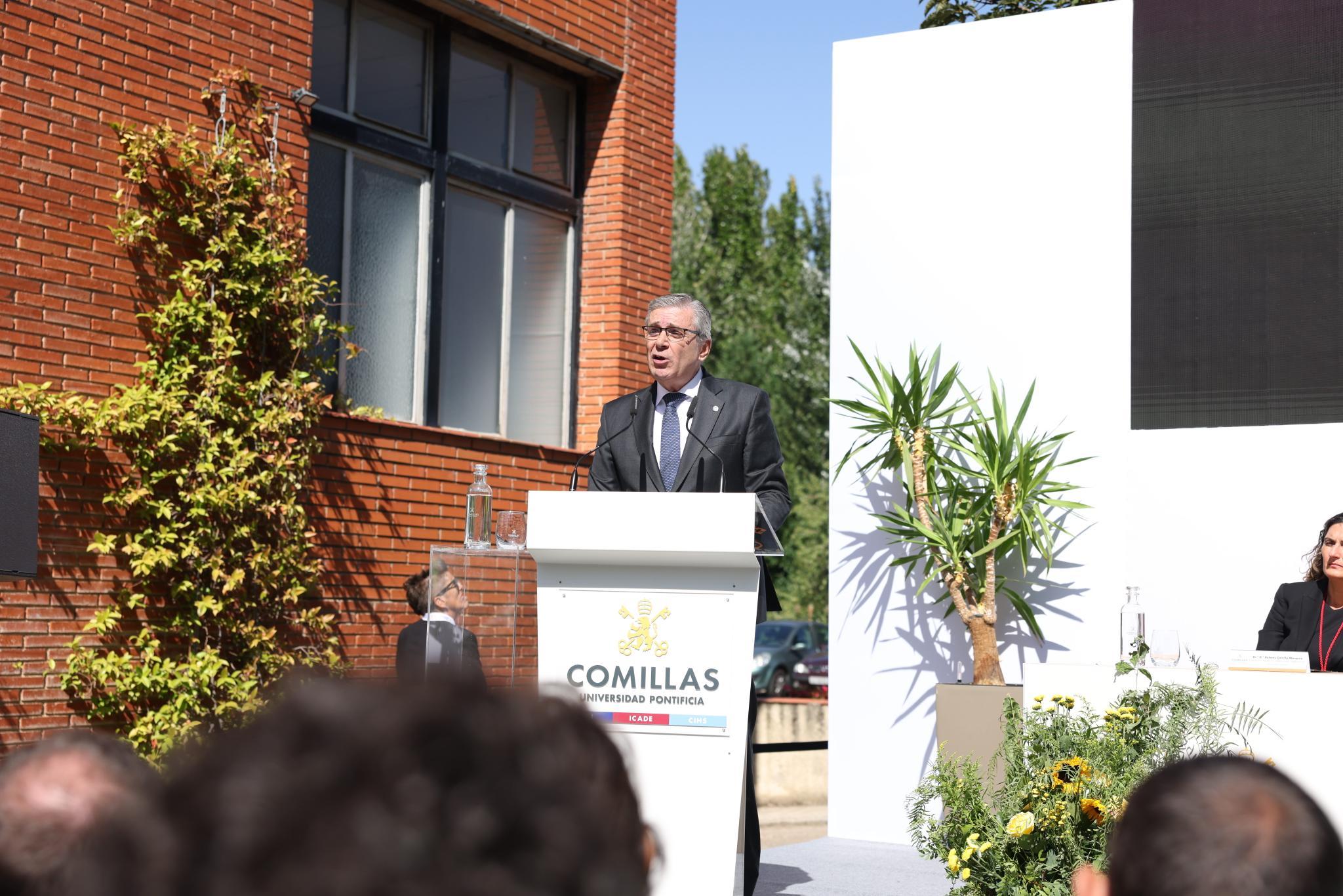 Un hombre habla desde un podio en un evento al aire libre en una institución educativa.