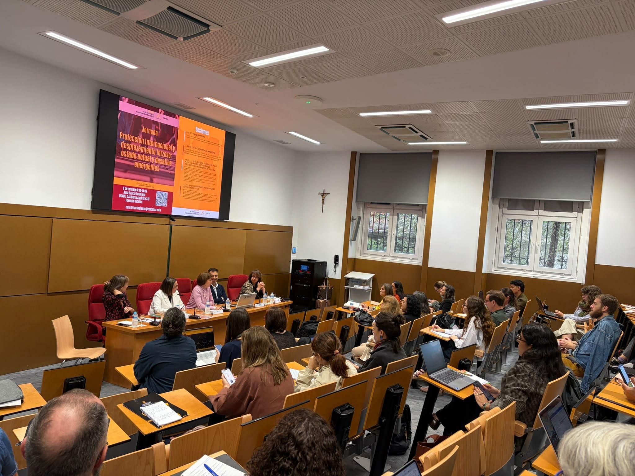 Una conferencia con un panel de presentadores frente a un público en un aula.