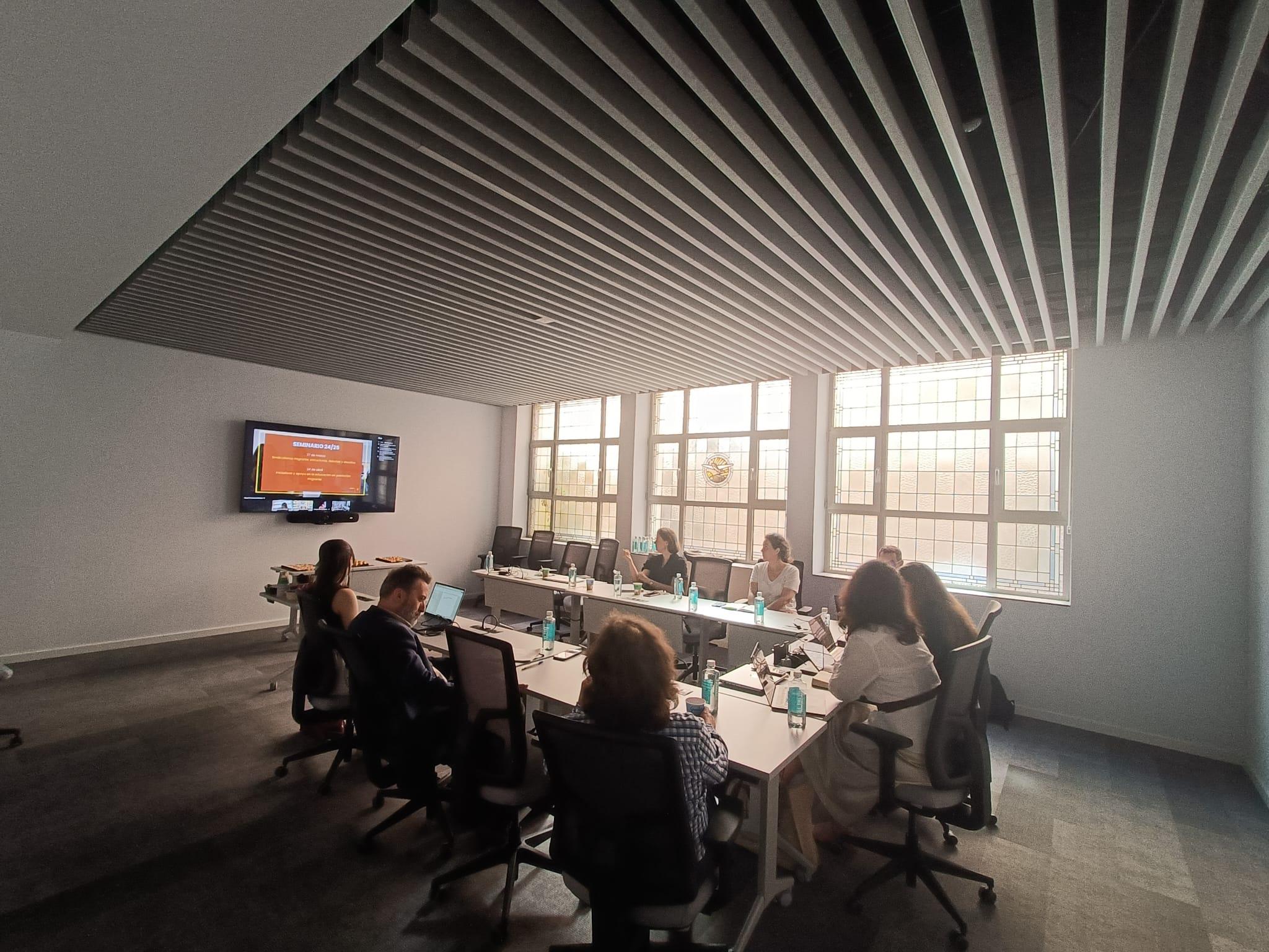 Una reunión en una sala moderna con varias personas sentadas alrededor de una mesa.
