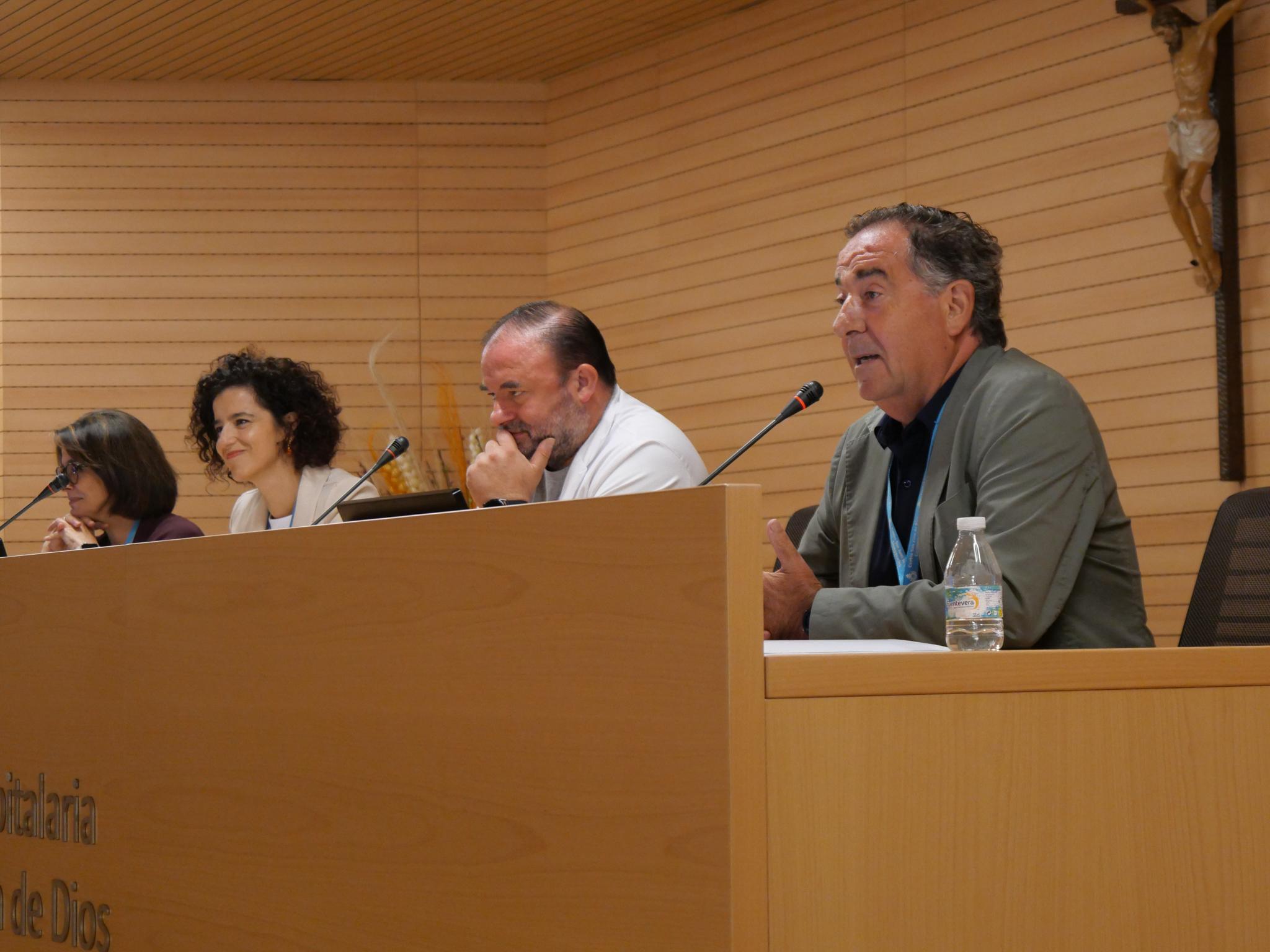 Una conferencia con cuatro ponentes sentados en una mesa, discutiendo temas de interés.
