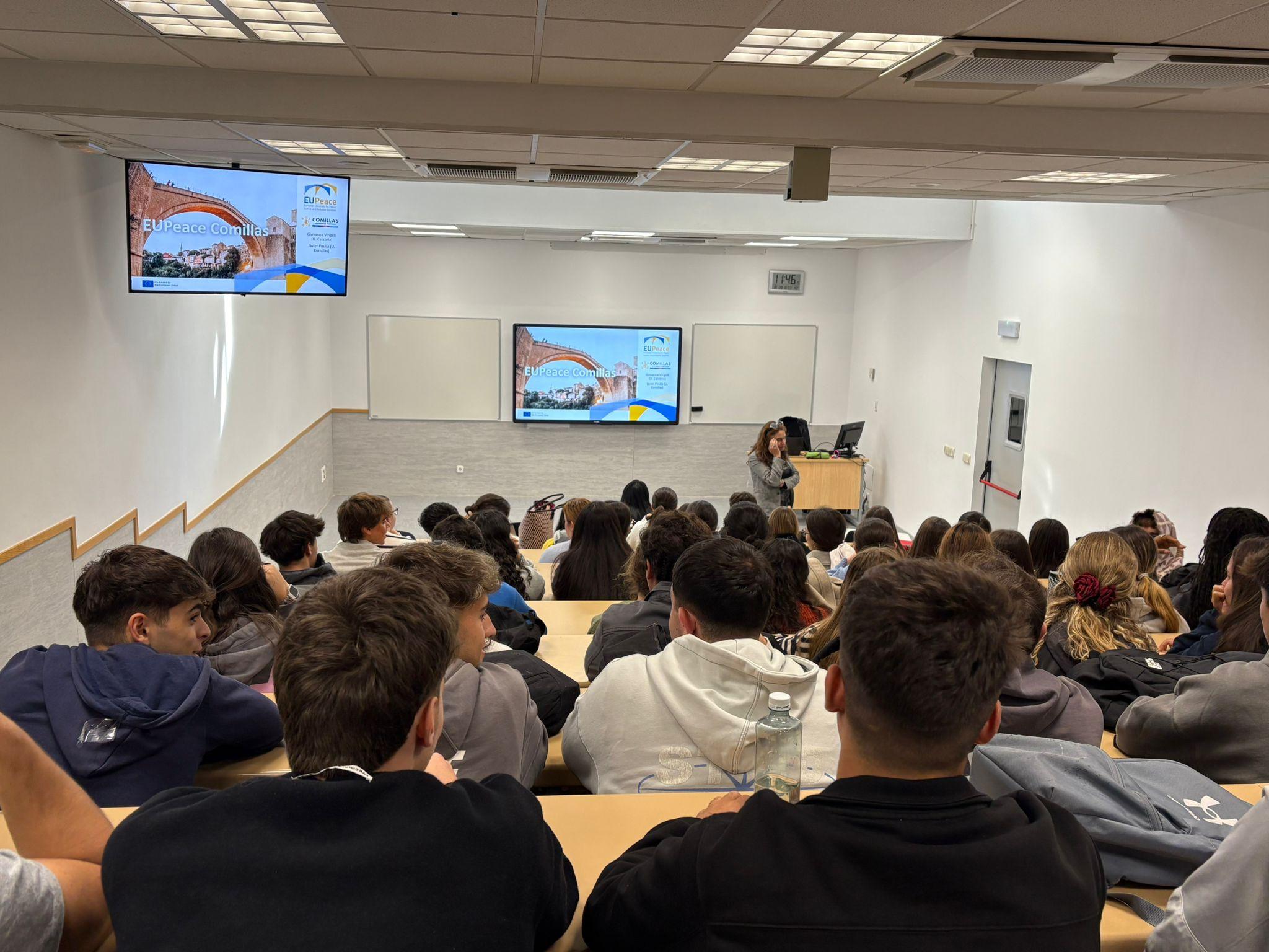 Una sala de clases con estudiantes prestando atención a una presentación.