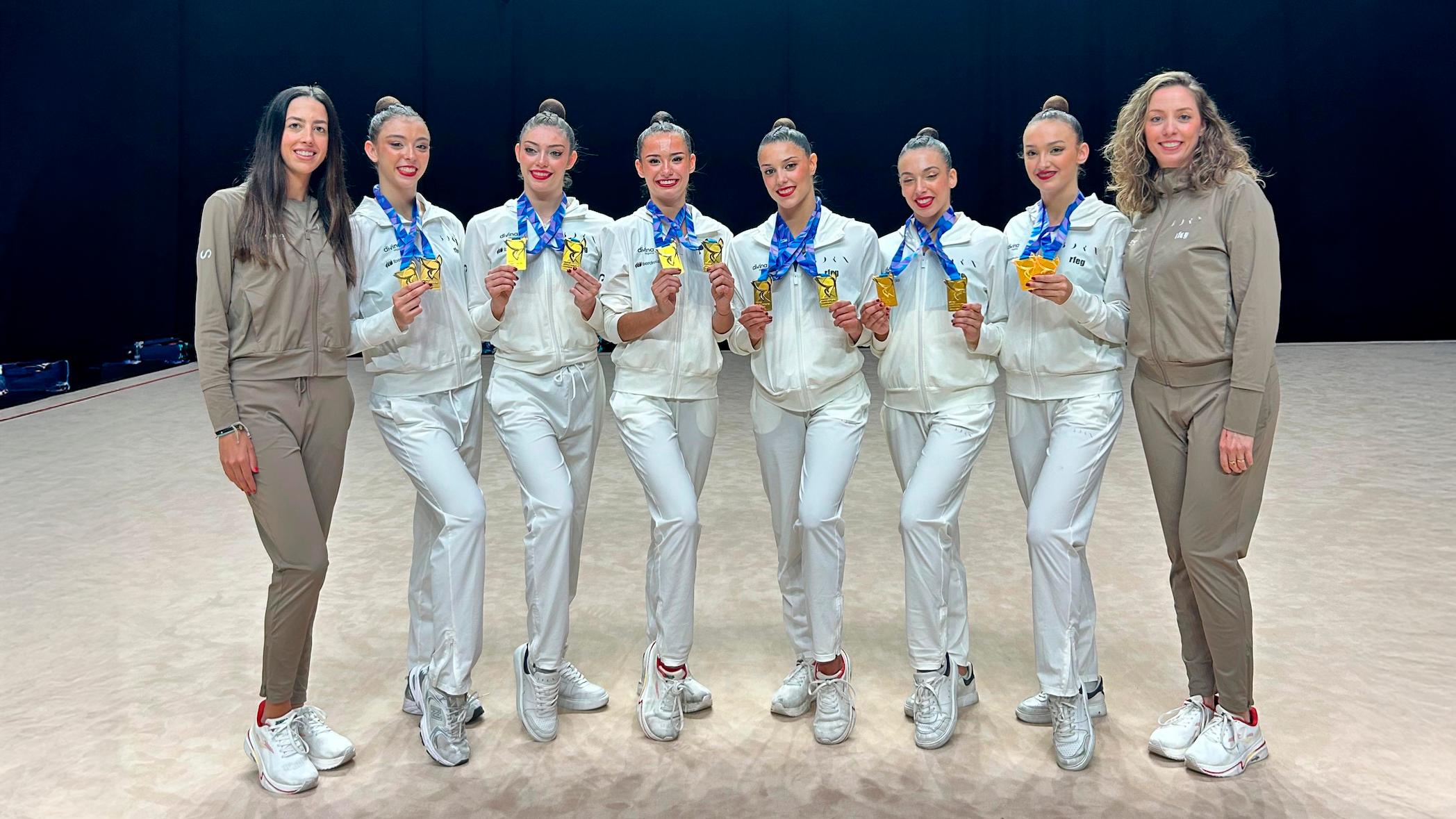 Un grupo de atletas posando juntas con medallas en un ambiente deportivo.