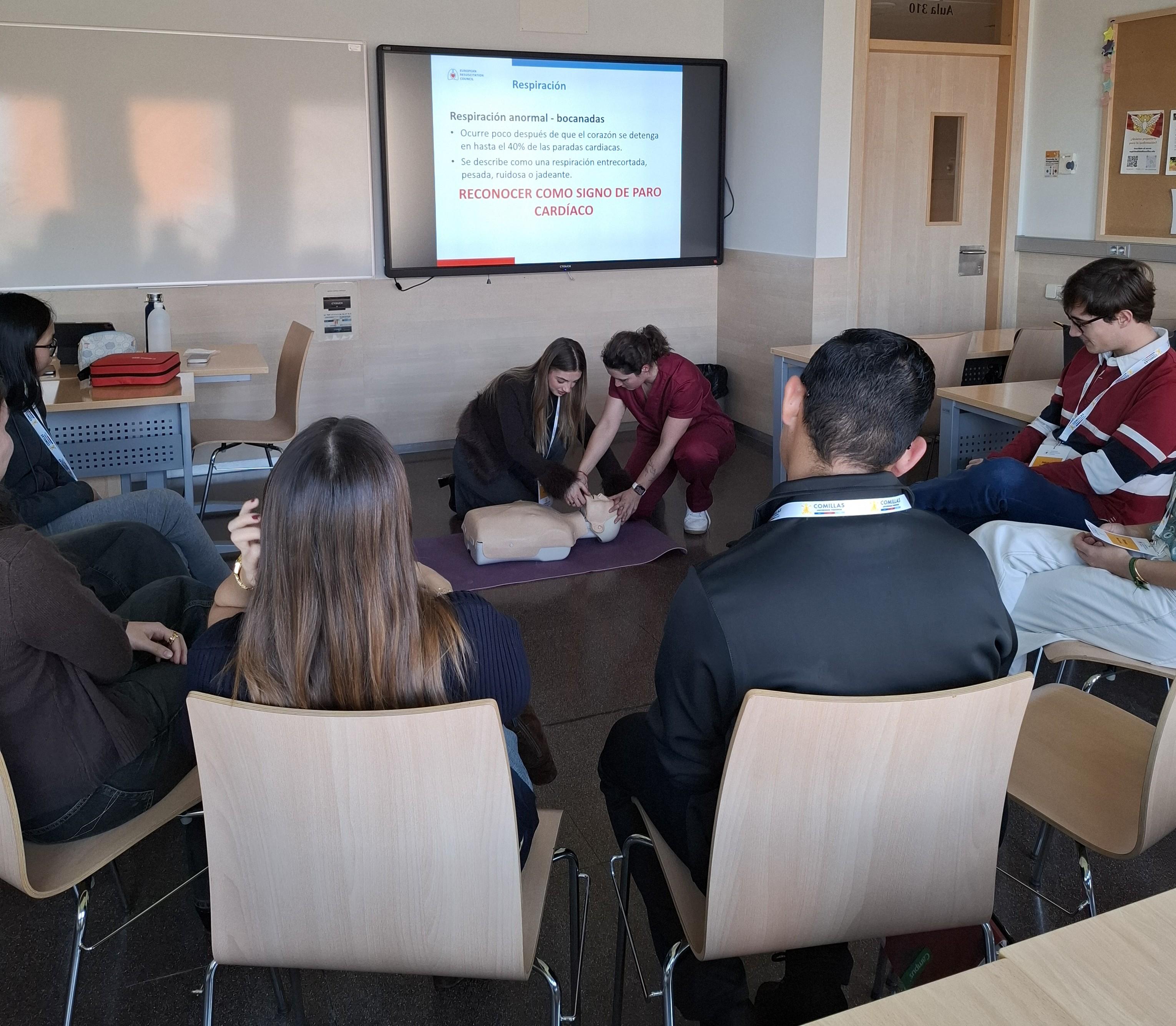 Un grupo de personas observa una demostración de primeros auxilios en un aula.