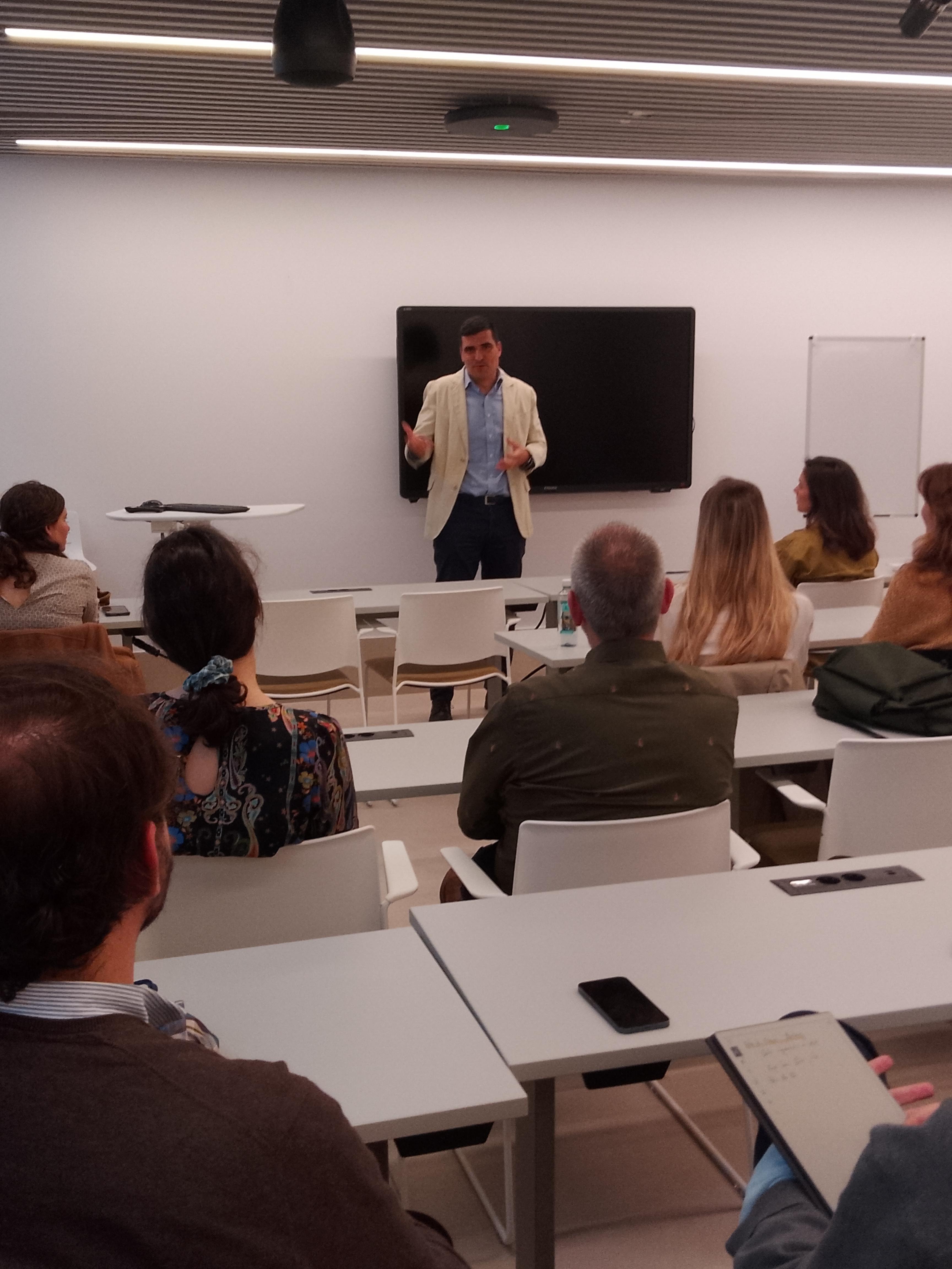 Un hombre está presentando frente a una audiencia en un aula moderna.