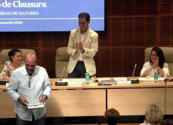 A man is receiving a certificate at a university event for seniors, as other attendees applaud for him.