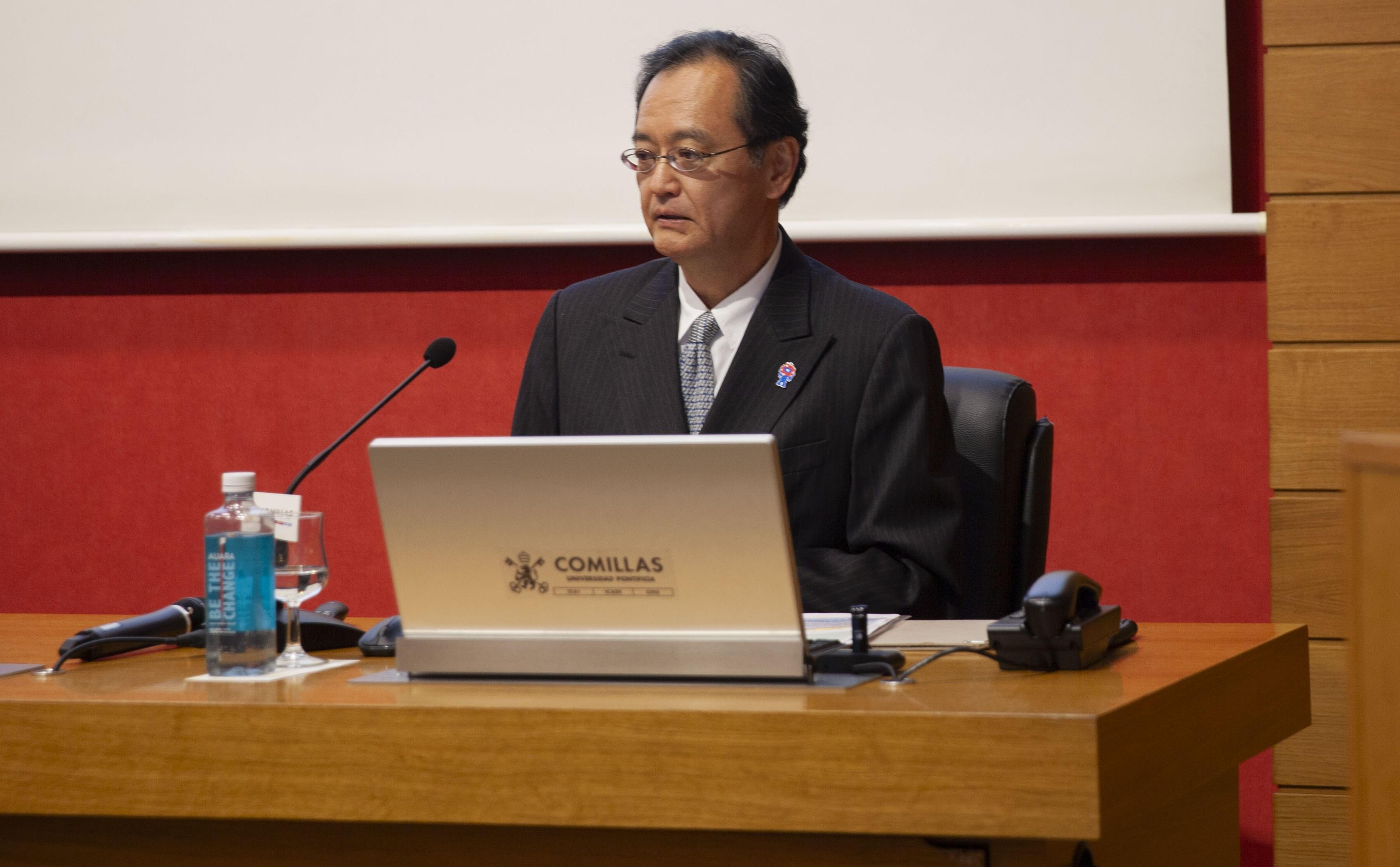 Un hombre está dando una conferencia en un auditorio con un portátil sobre una mesa.