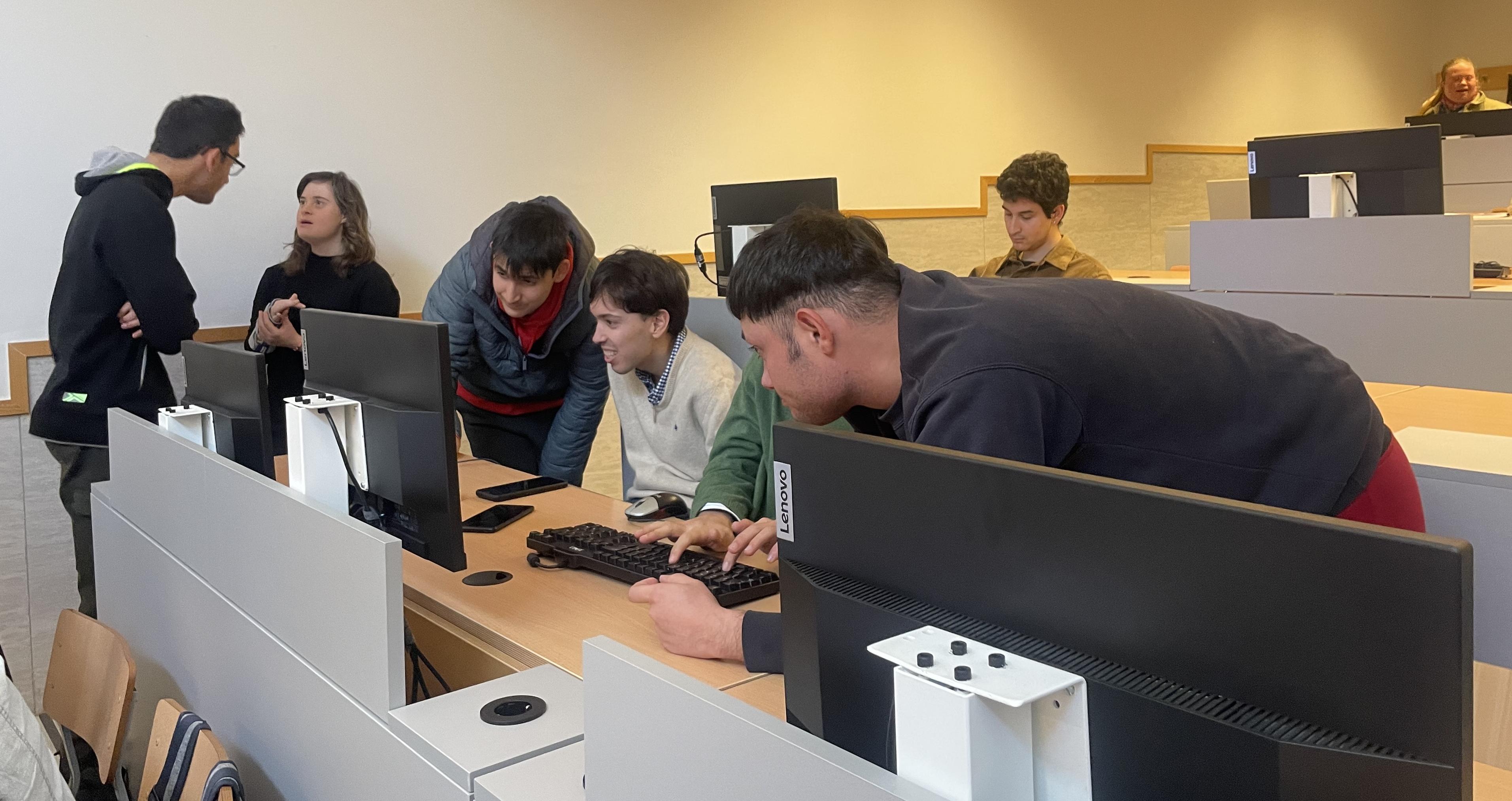 Un grupo de personas colaborando en un aula con ordenadores.