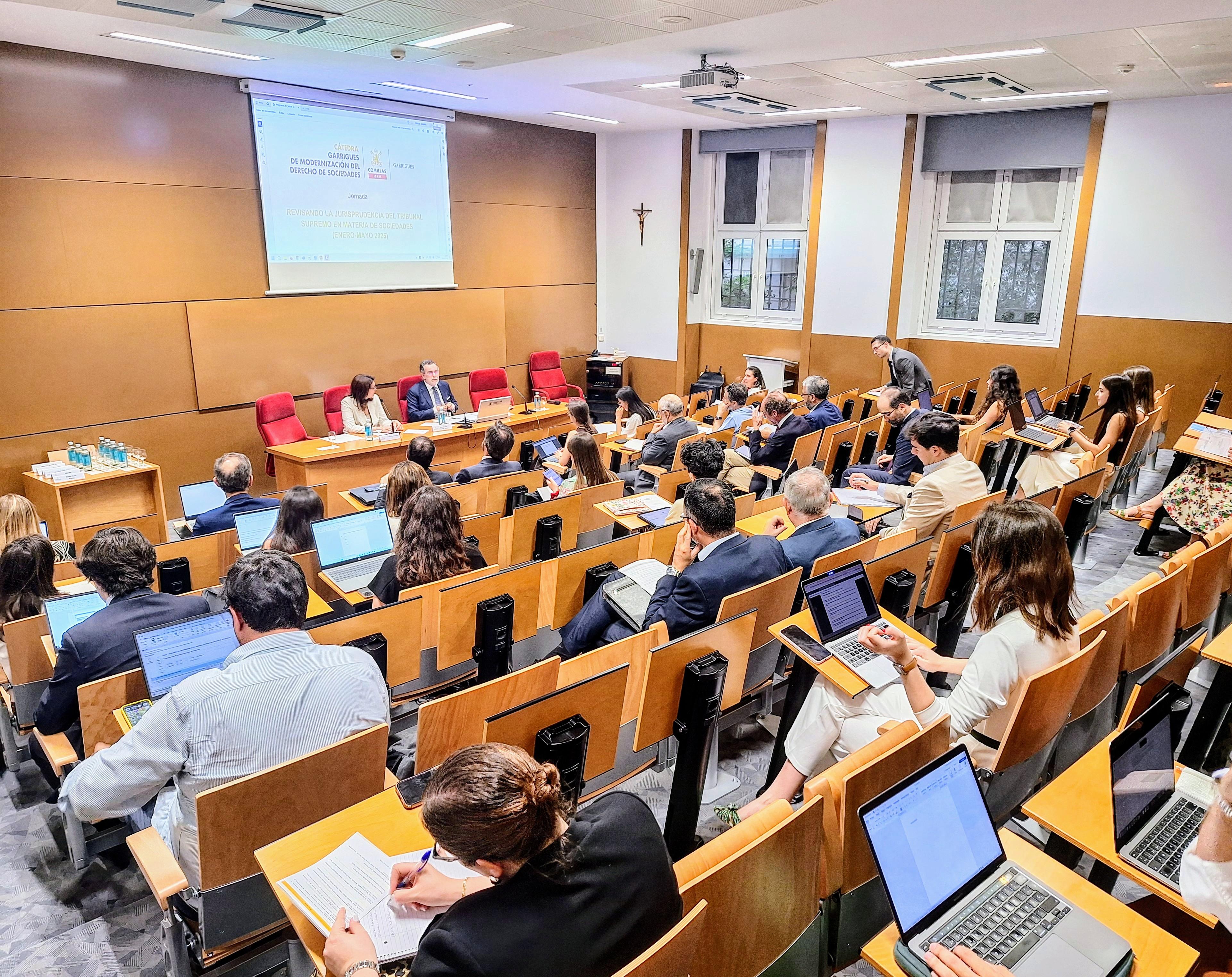 Una sala de conferencias con un grupo de personas sentadas, prestando atención a un panel de discusión.