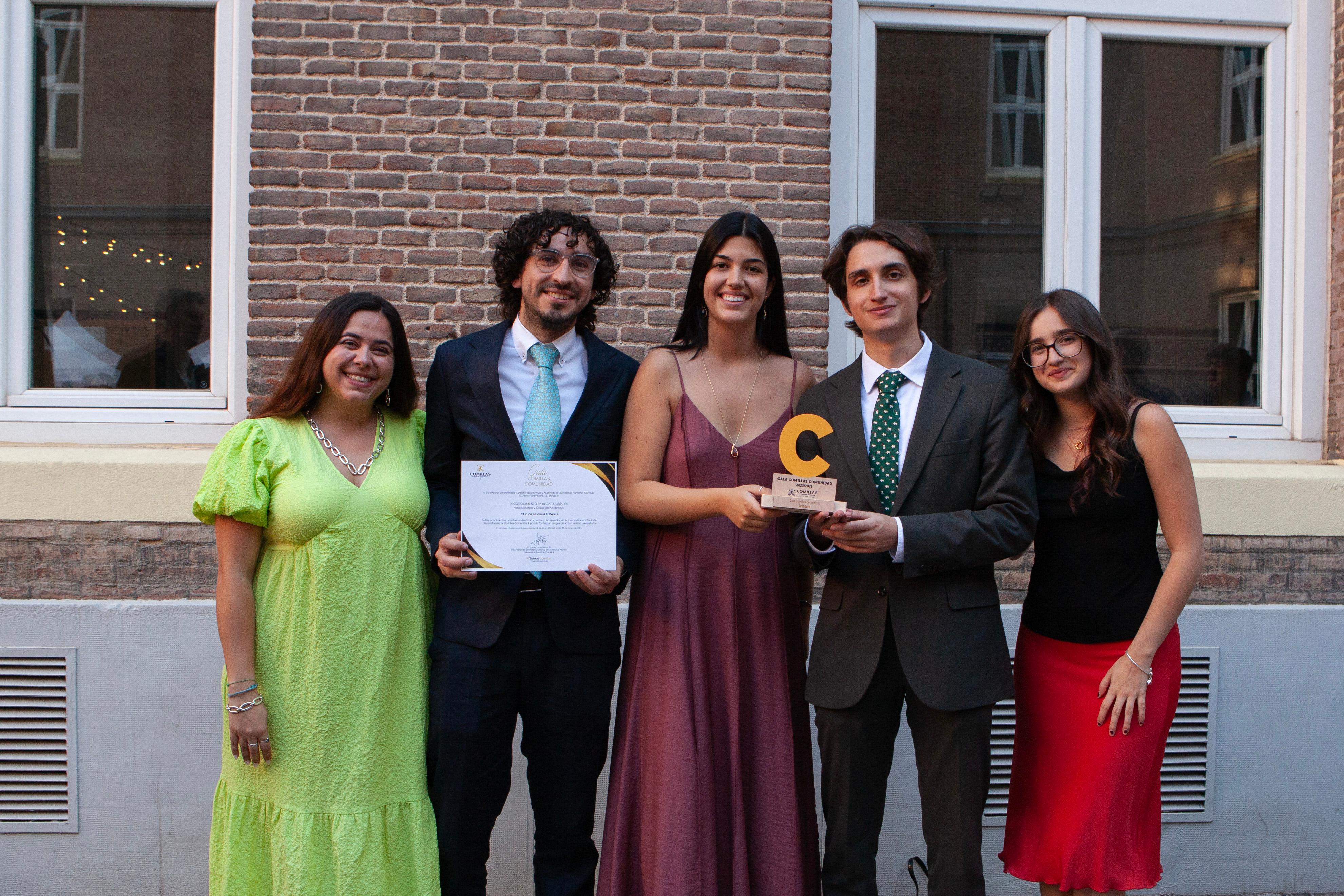 Un grupo de cinco personas posa sonriente después de recibir un reconocimiento en un evento formal.