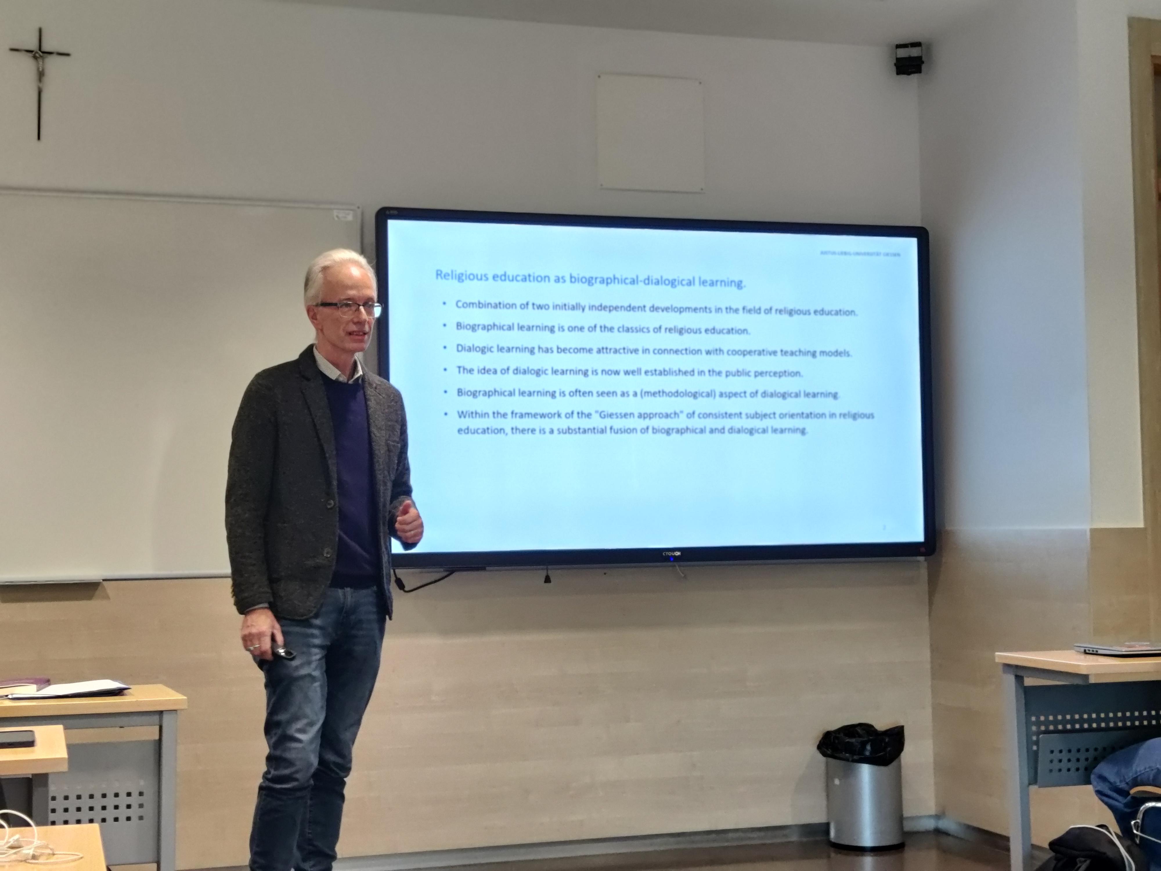 Un hombre presenta información sobre el aprendizaje biográfico en un aula con una pantalla de proyección.