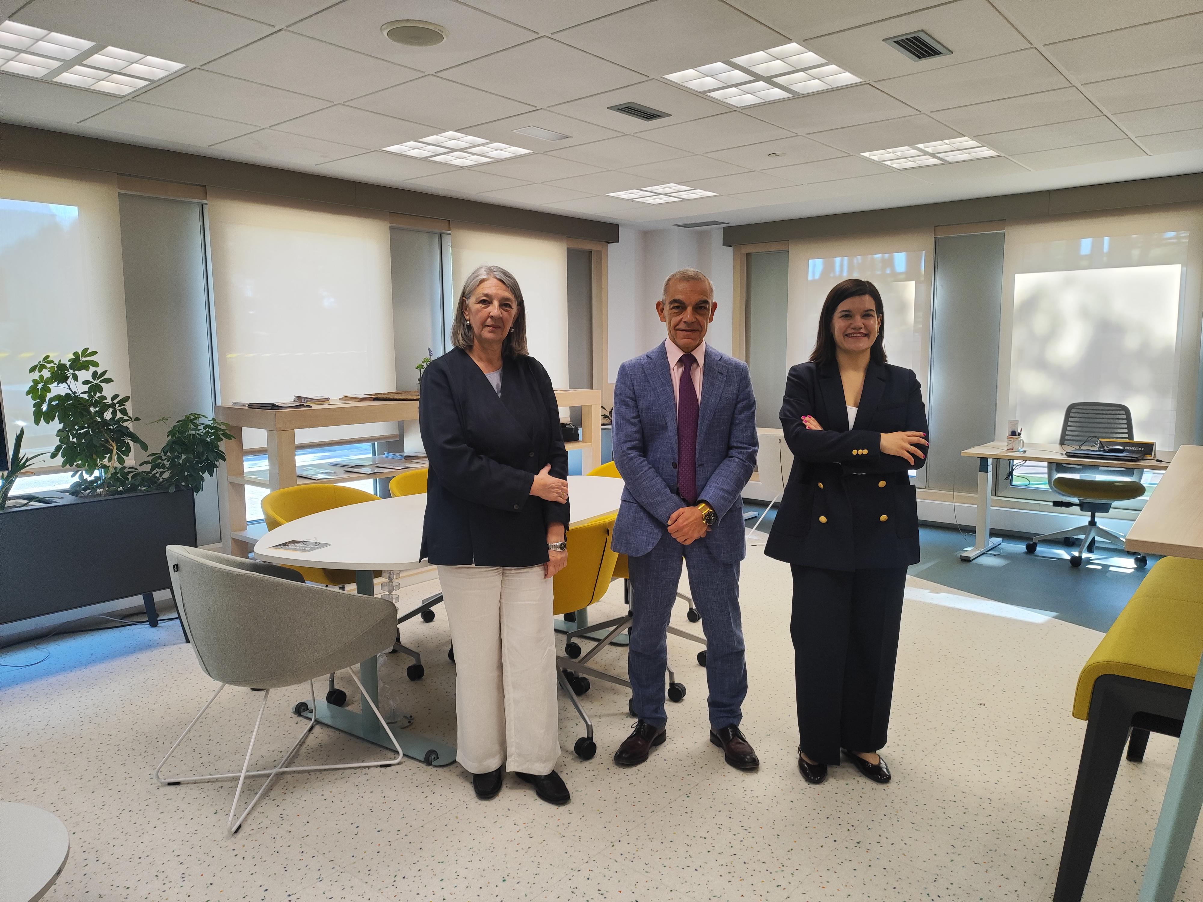 Tres personas posan en una moderna oficina con mesas y sillas.