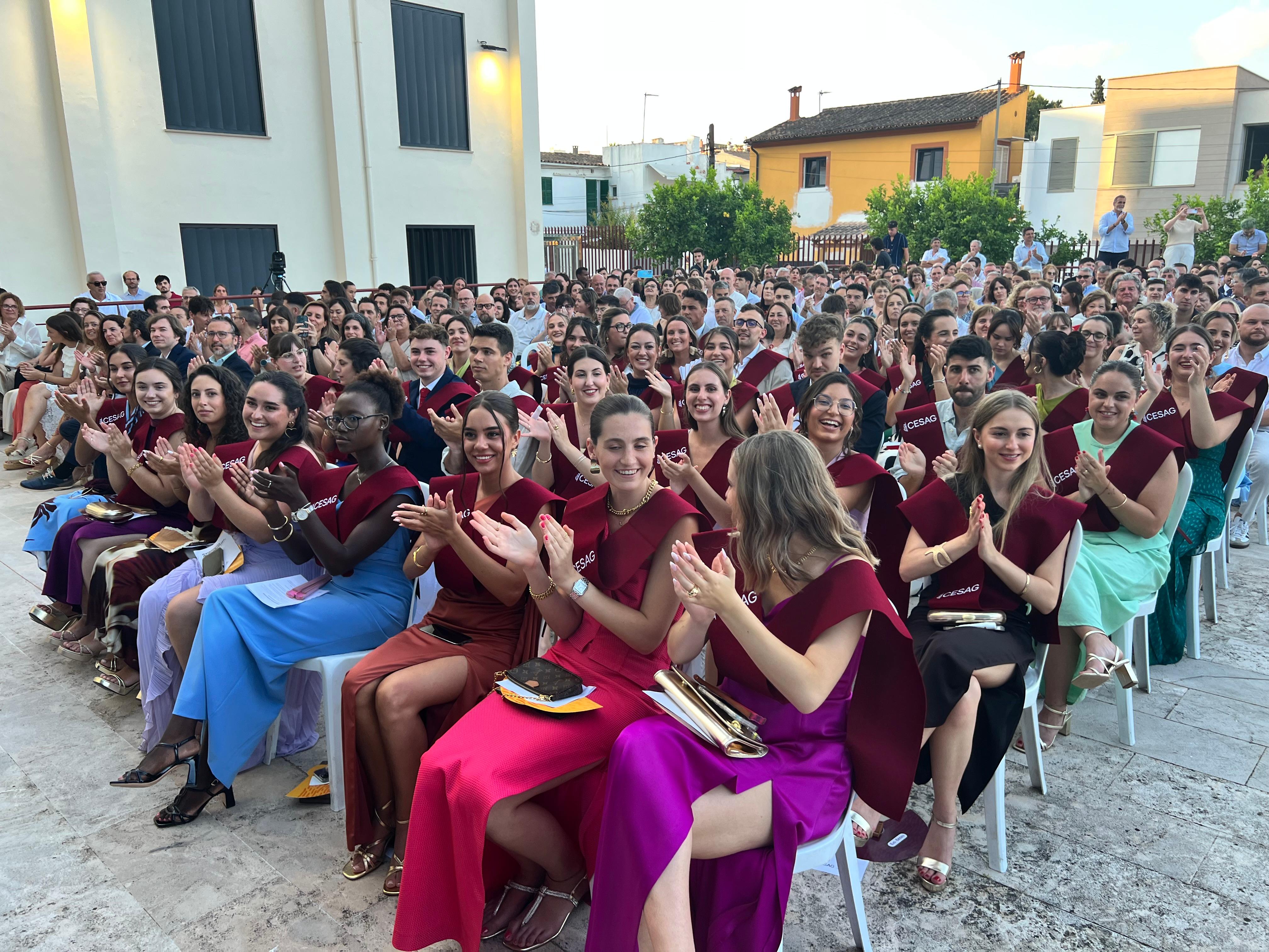 Un gran grupo de graduados aplaudiendo en una ceremonia al aire libre.
