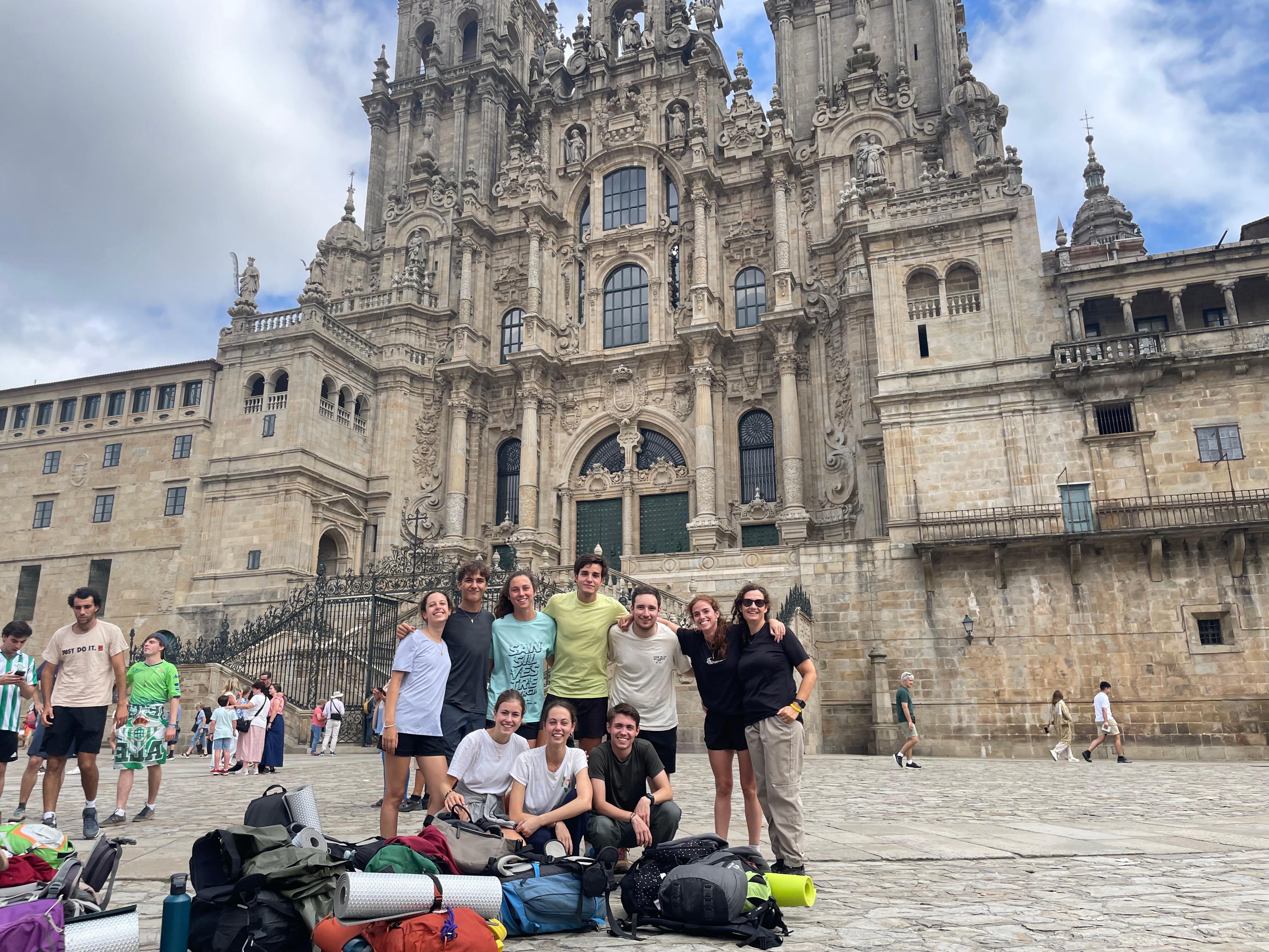 Un grupo de personas sonrientes posa frente a una impresionante fachada arquitectónica en un día nublado.