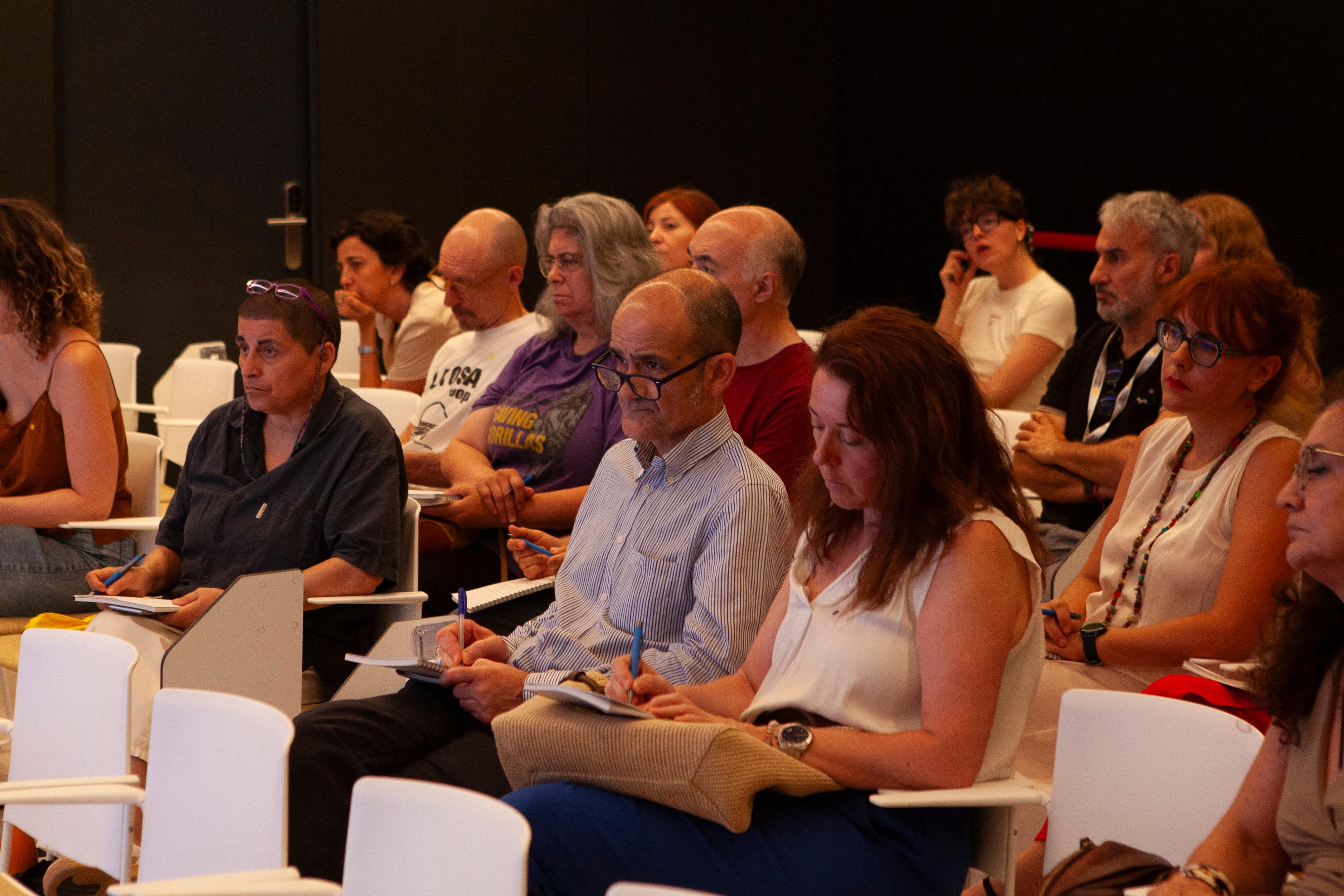 Un grupo de personas sentadas en una sala durante una conferencia o charla, tomando notas.