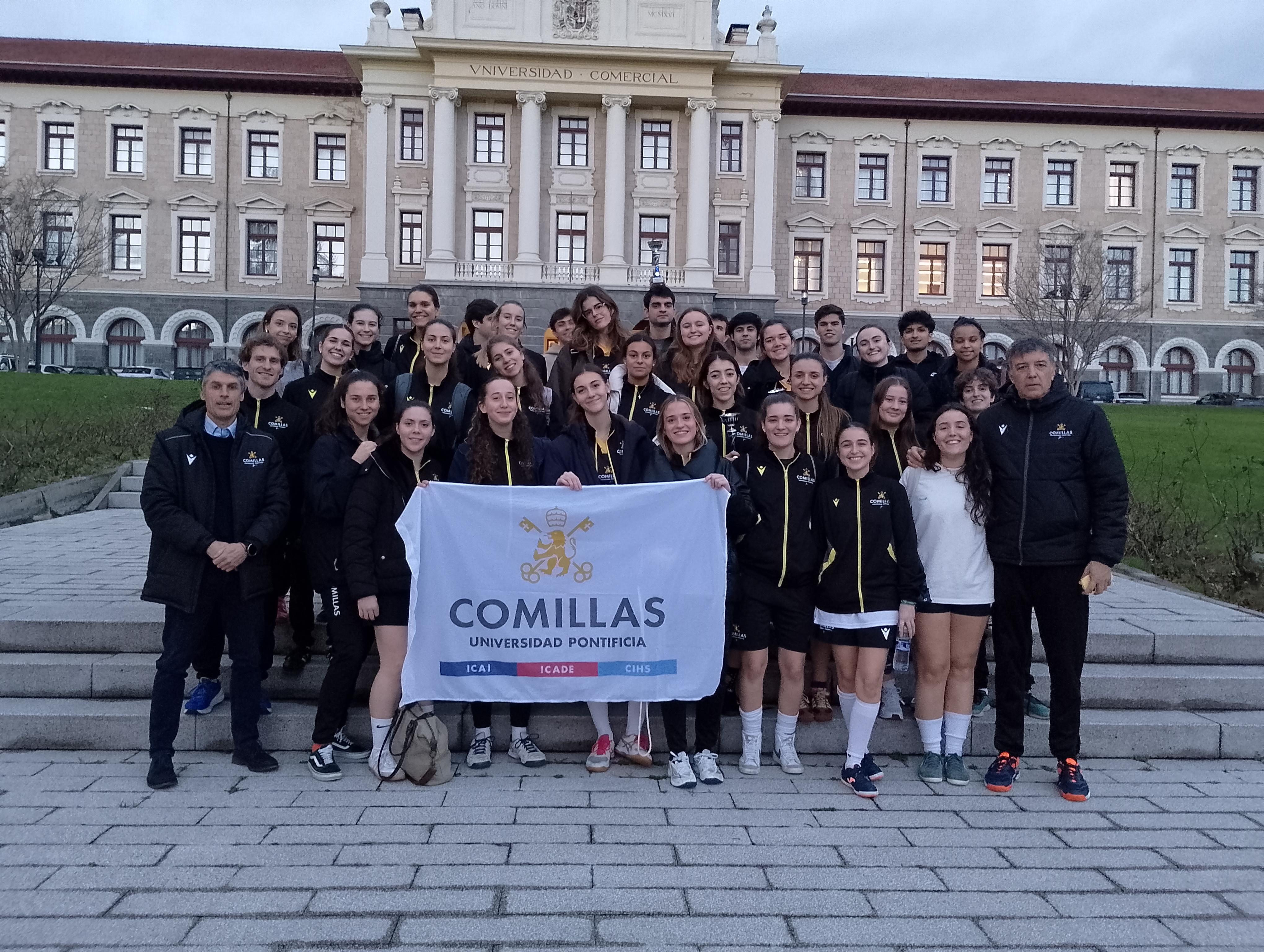 Fotografía de un grupo grande de estudiantes de la Universidad Pontificia Comillas posando con una bandera en un campus universitario.