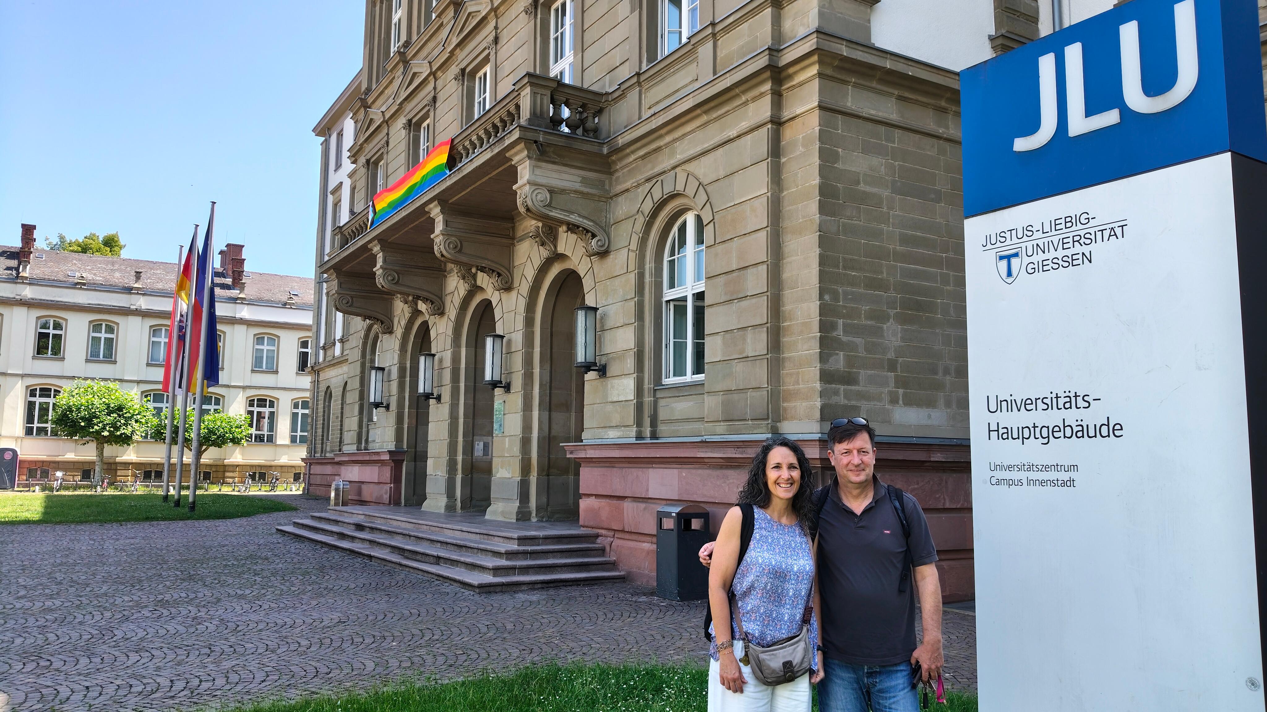 Una pareja sonriente posa frente al edificio principal de la Universidad Justus Liebig en Giessen, Alemania.
