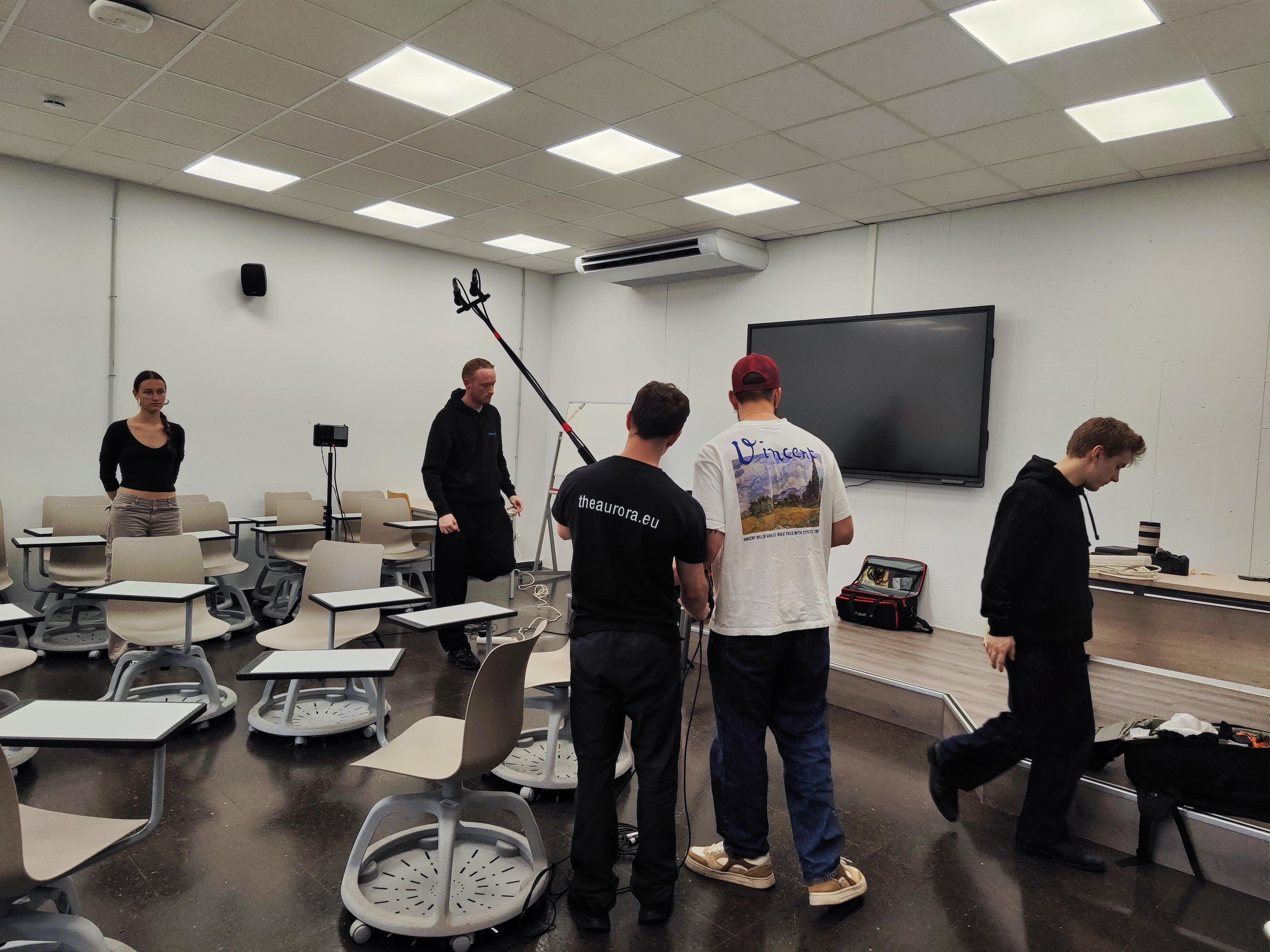 Un grupo de personas se prepara en un aula equipada para una grabación o presentación.