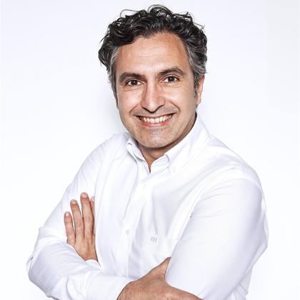 A cheerful man in a white shirt smiling confidently at the camera with his arms crossed.
