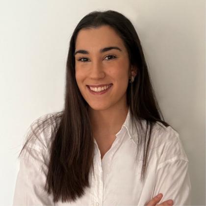 Una joven sonriente con una camisa blanca posando frente a un fondo blanco.