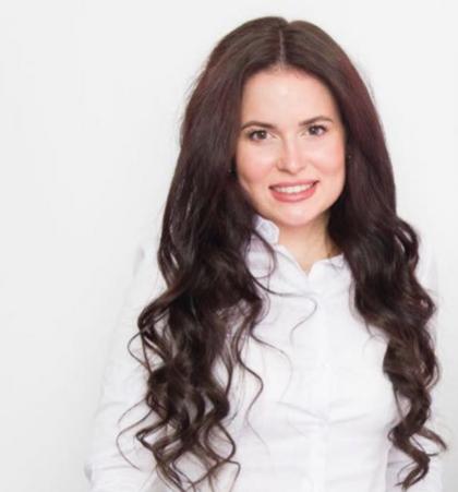 Mujer sonriente con cabello largo y ondulado posando en una camisa blanca sobre fondo blanco.