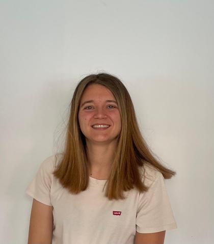 A young woman smiling in front of a white background, wearing a white t-shirt with a red logo.